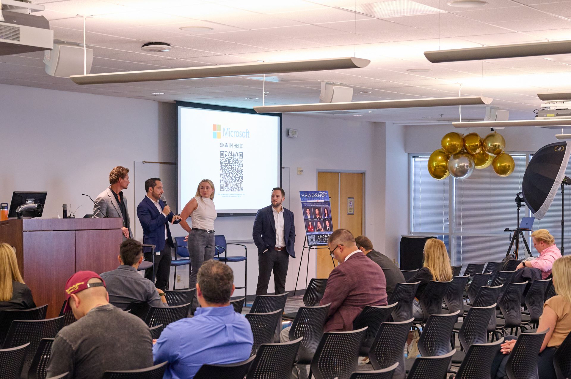 A group of people are sitting in chairs in front of a projector screen.