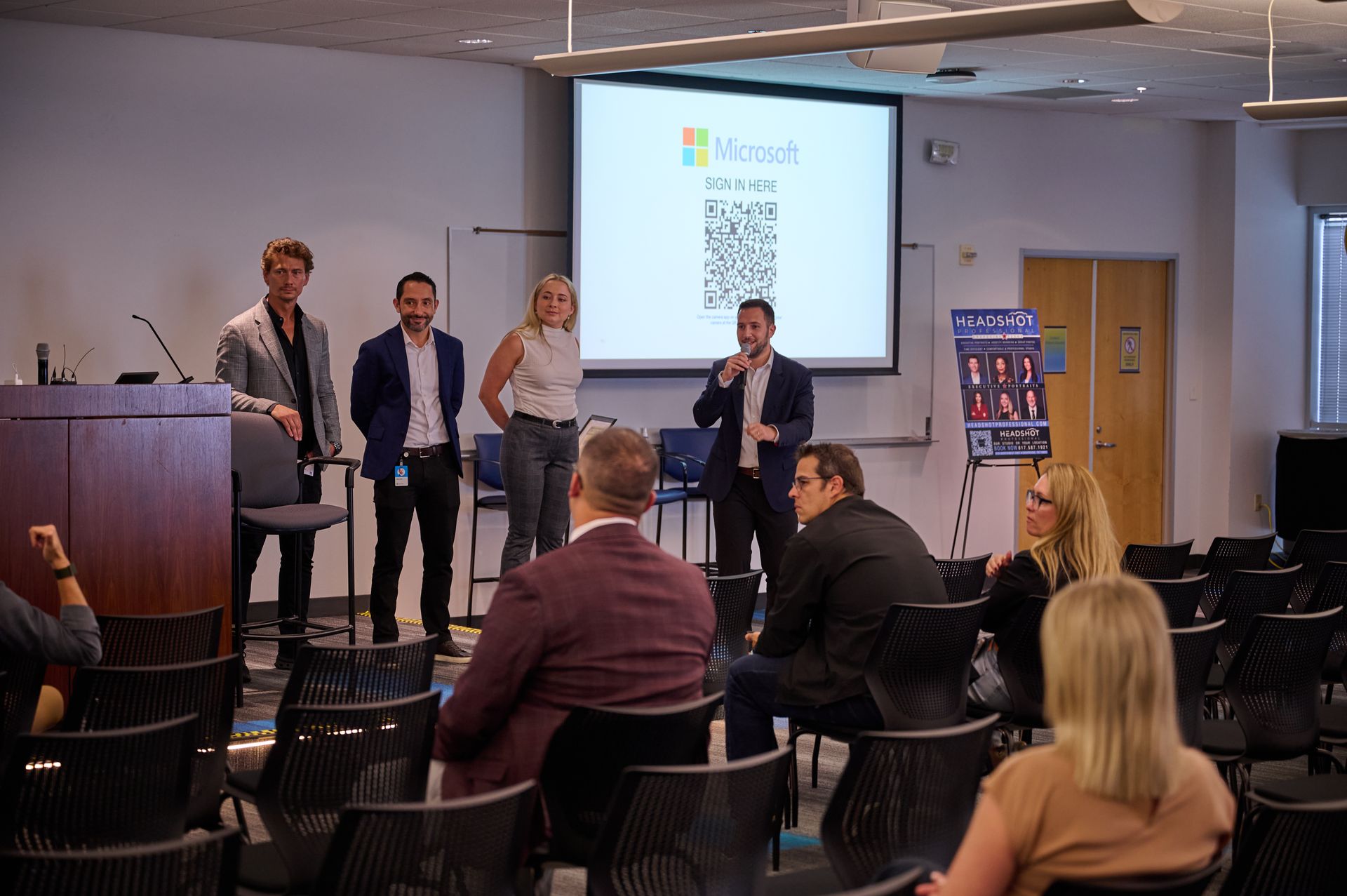 A group of people are sitting in chairs in front of a projector screen.