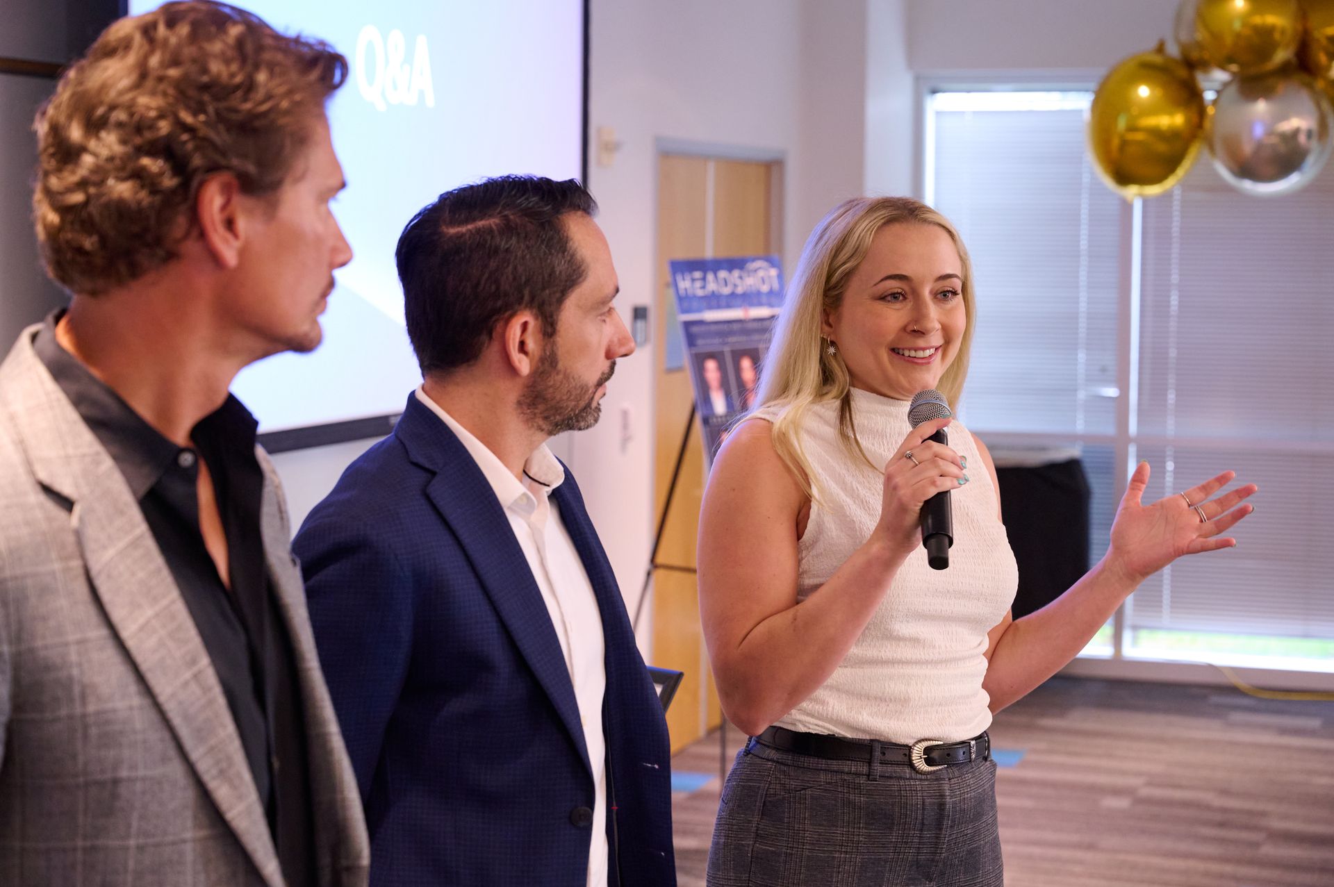A woman is holding a microphone while standing next to two men in suits.