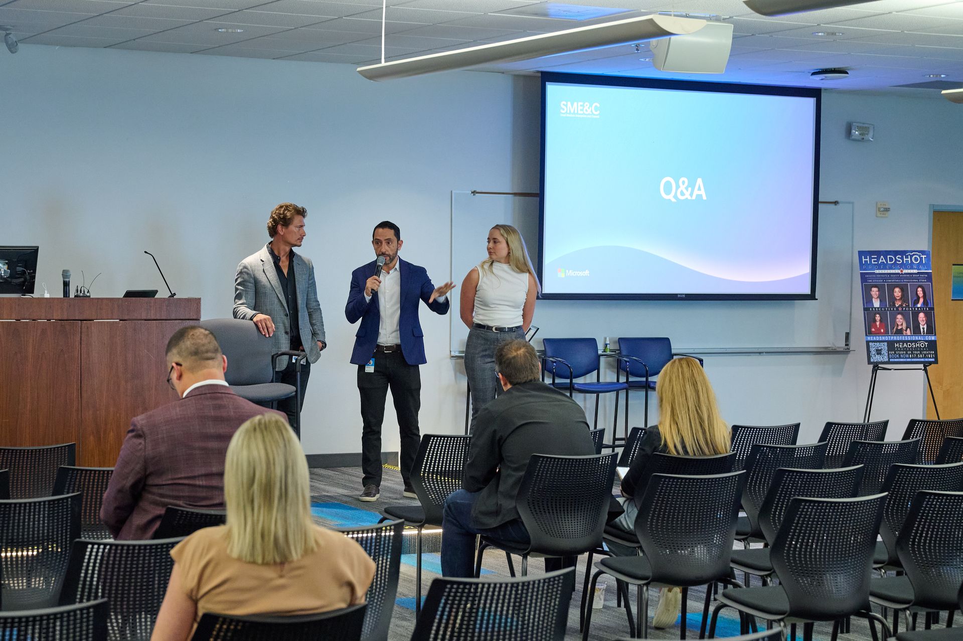 A group of people are sitting in chairs in front of a projector screen.