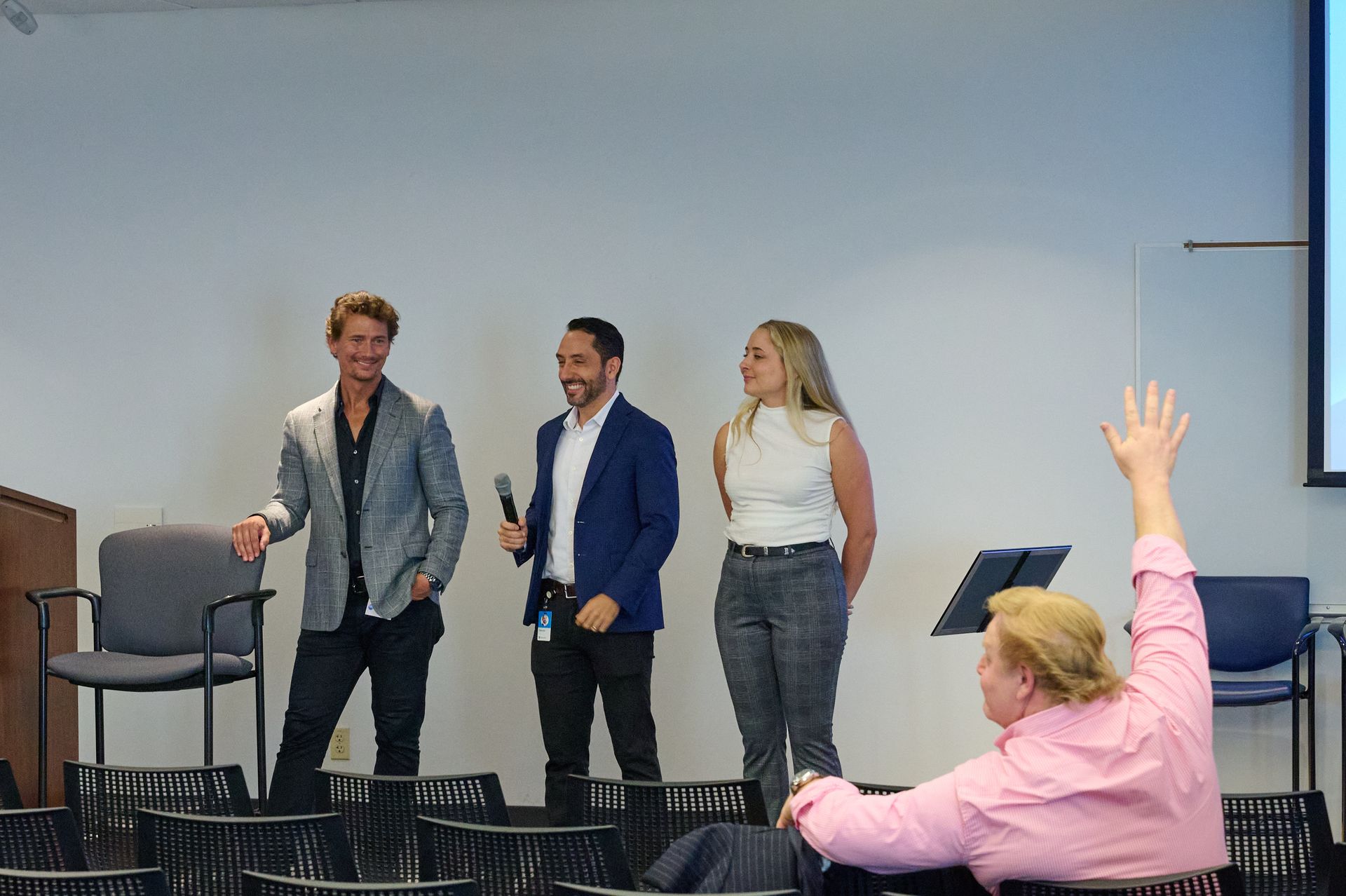 A man in a pink shirt is raising his hand to answer a question.