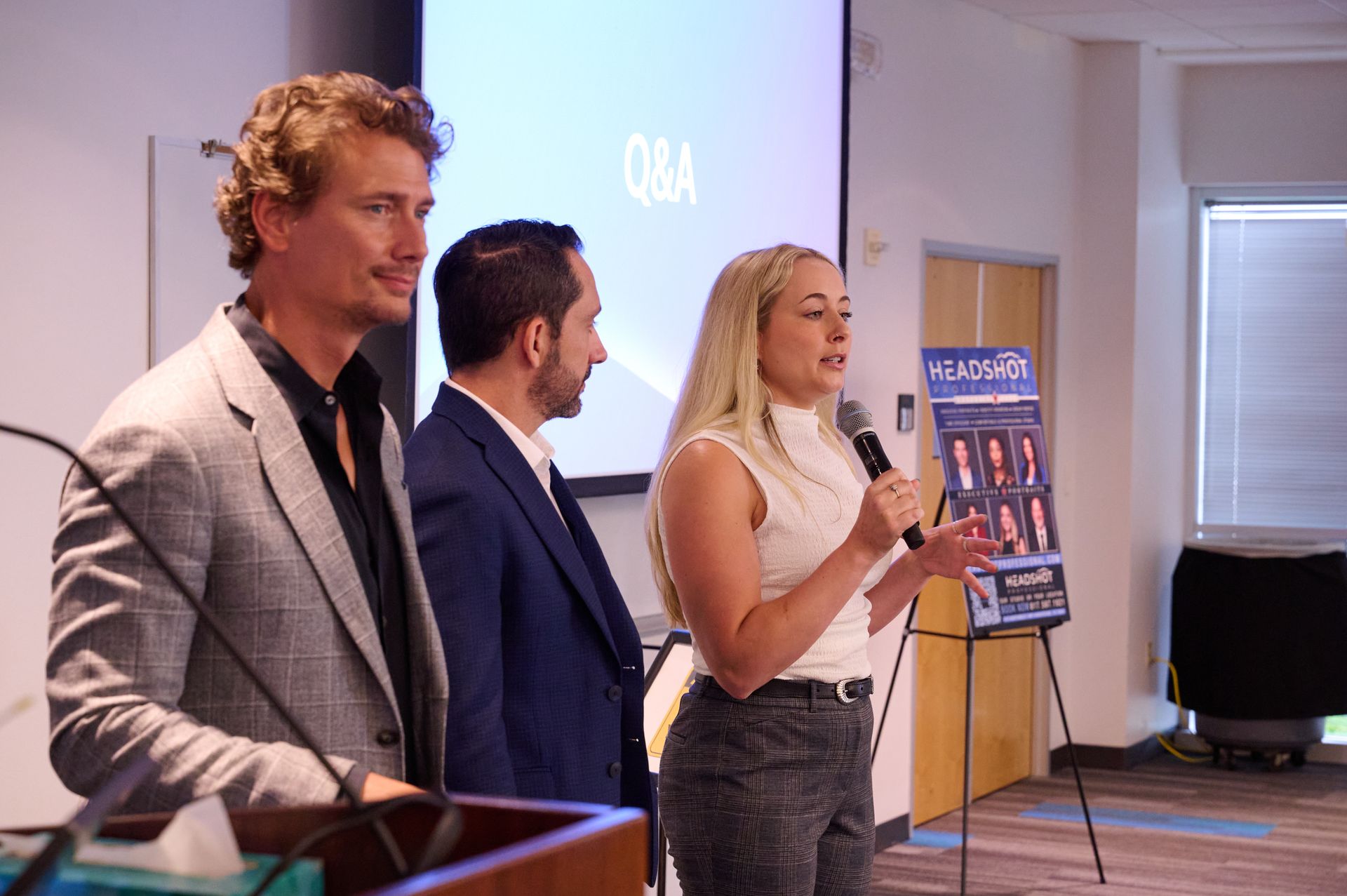 A woman is speaking into a microphone while two men stand behind her.