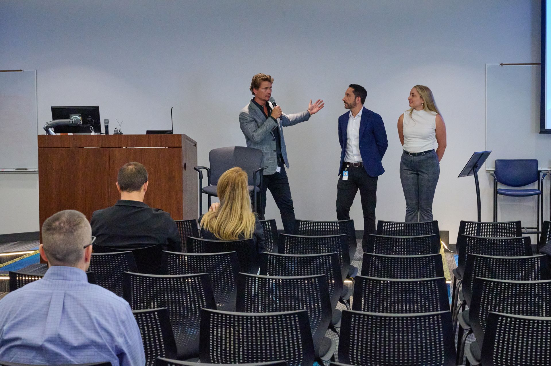 A group of people are standing in front of a podium in a lecture hall.
