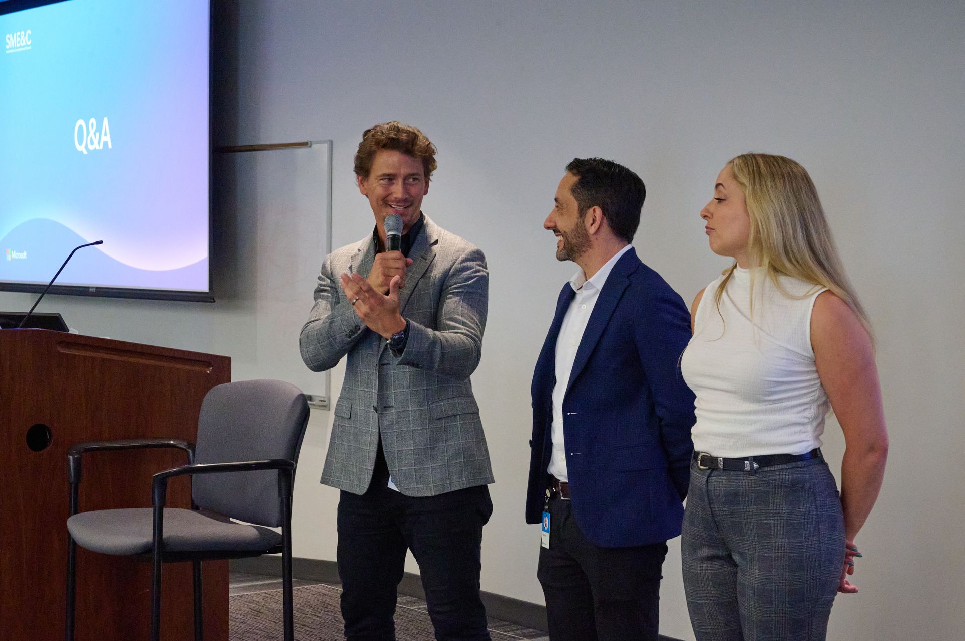 A man is speaking into a microphone while two other people stand behind him.