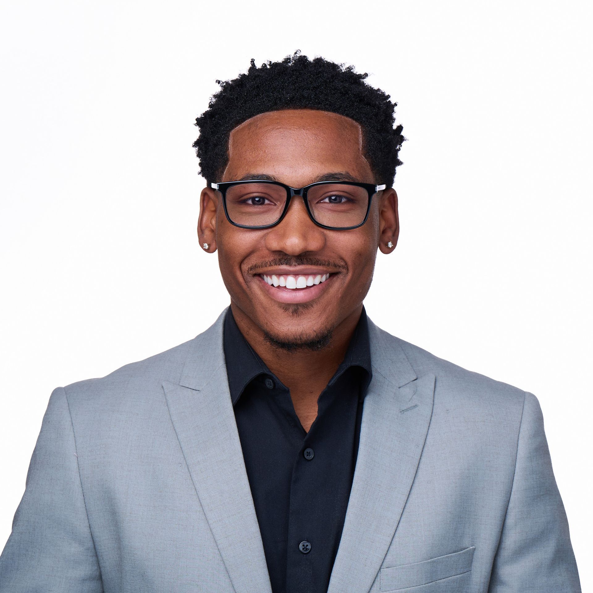 Portrait of a smiling man in glasses wearing a light gray blazer and black shirt on a white background