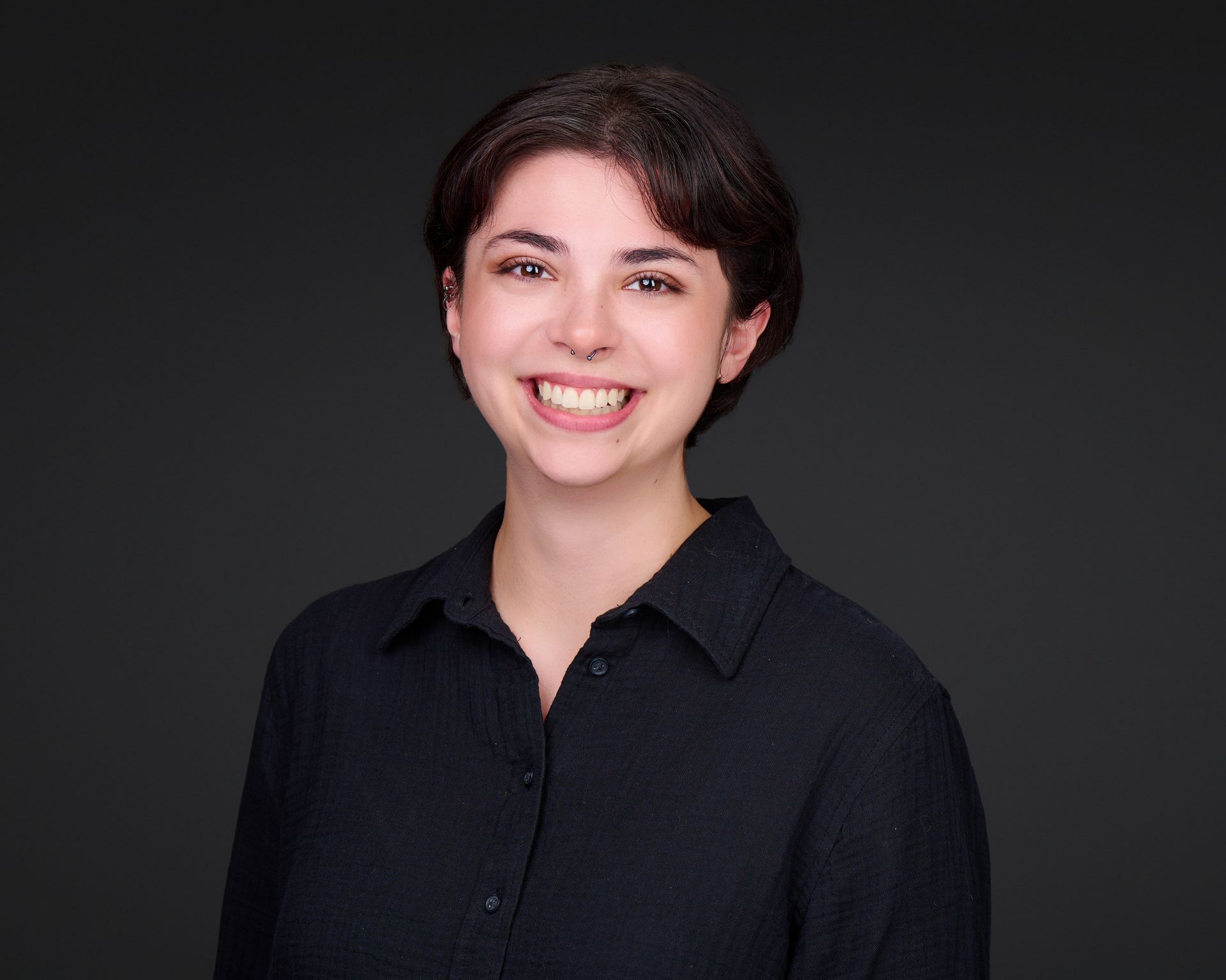 Smiling person in a black collared shirt against a dark gray background