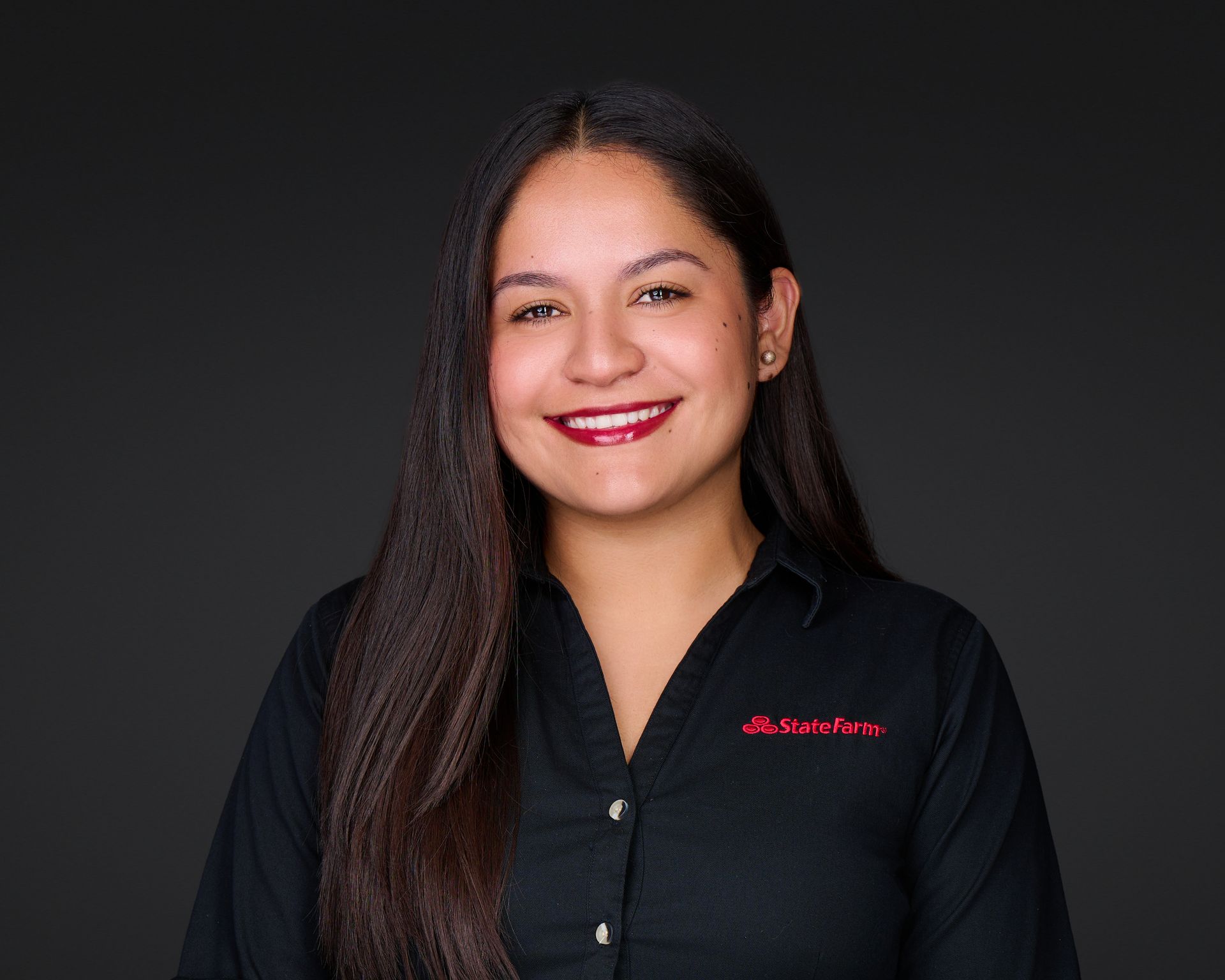 Smiling woman in a black shirt with red logo, standing against a dark background.