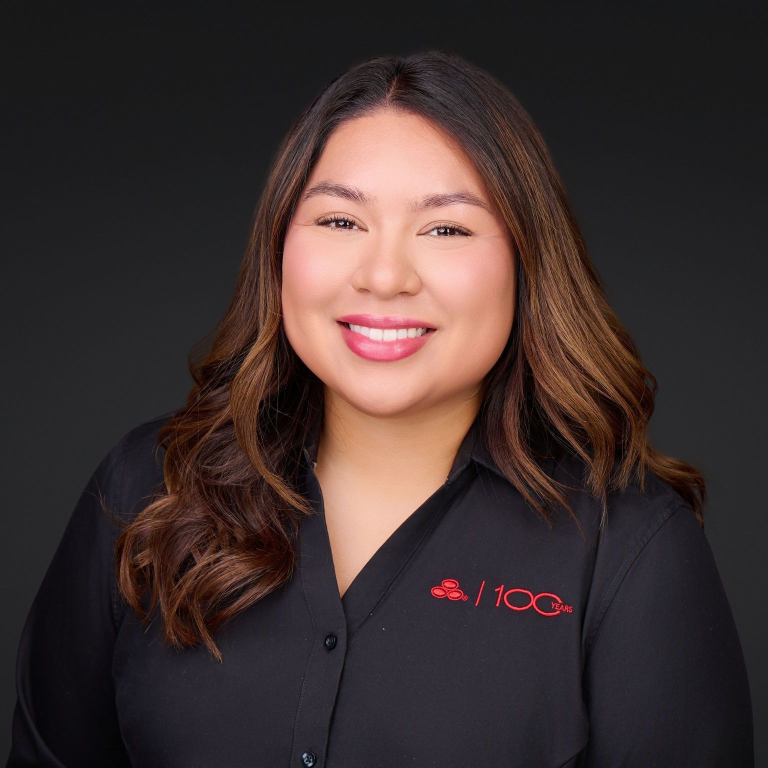 Smiling person in a black shirt with a red logo against a dark background