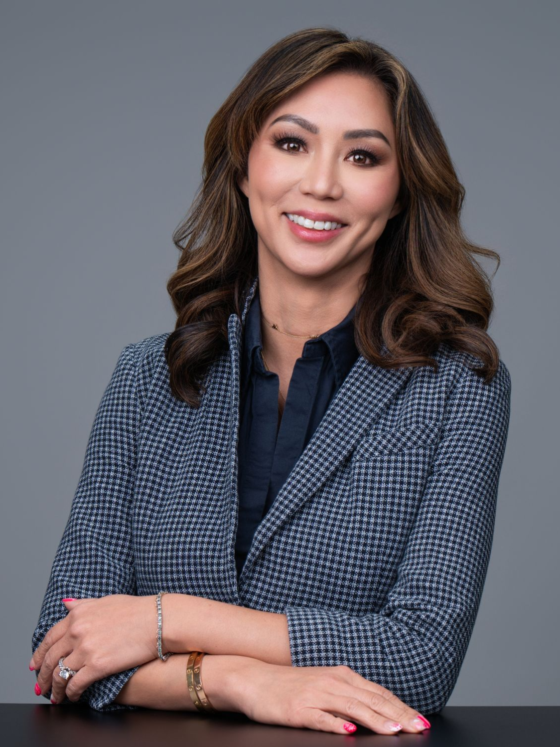 Portrait of a smiling woman in a blue blazer, leaning on a table against a gray background