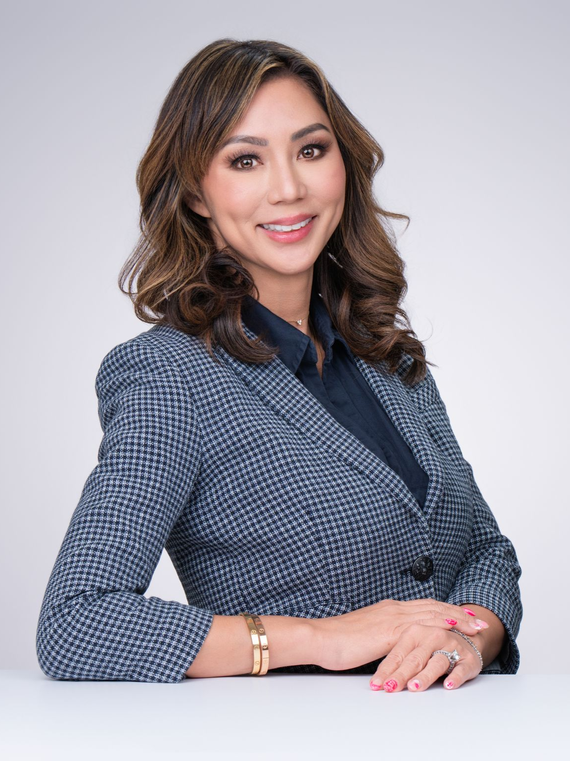 Portrait of a smiling woman in a blue patterned blazer, seated against a light gray background