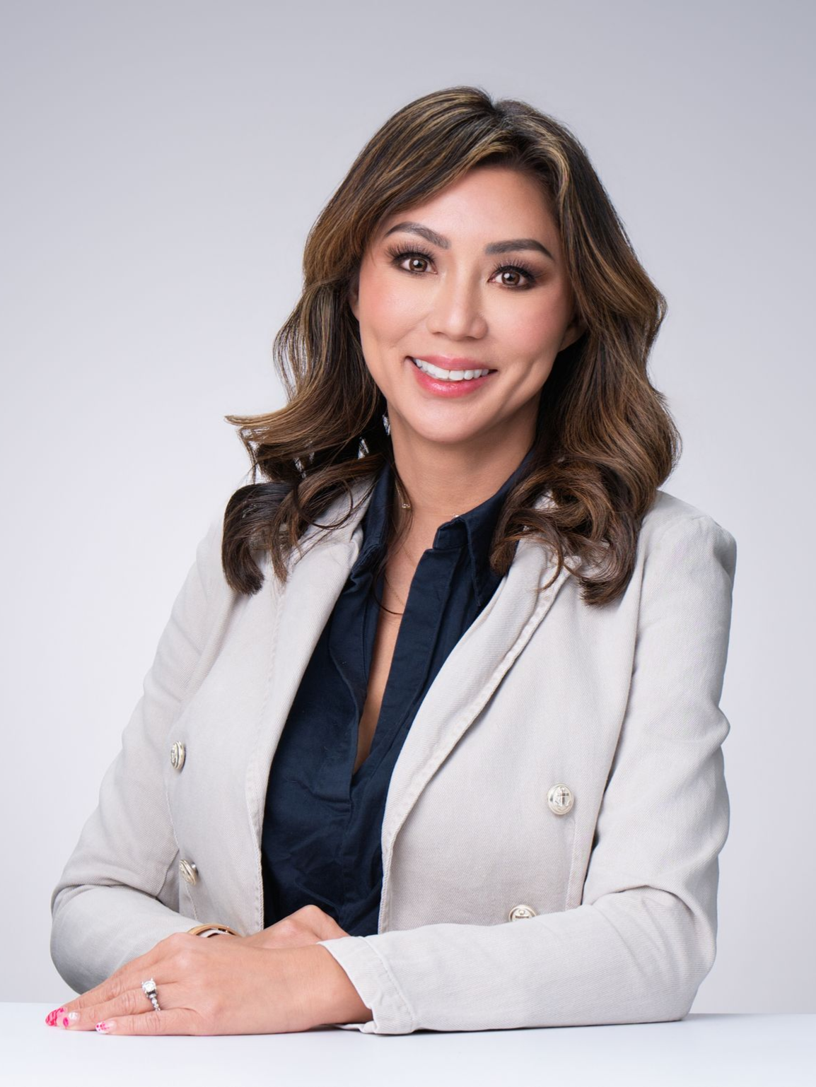Professional portrait of a smiling woman in a light gray blazer against a neutral background