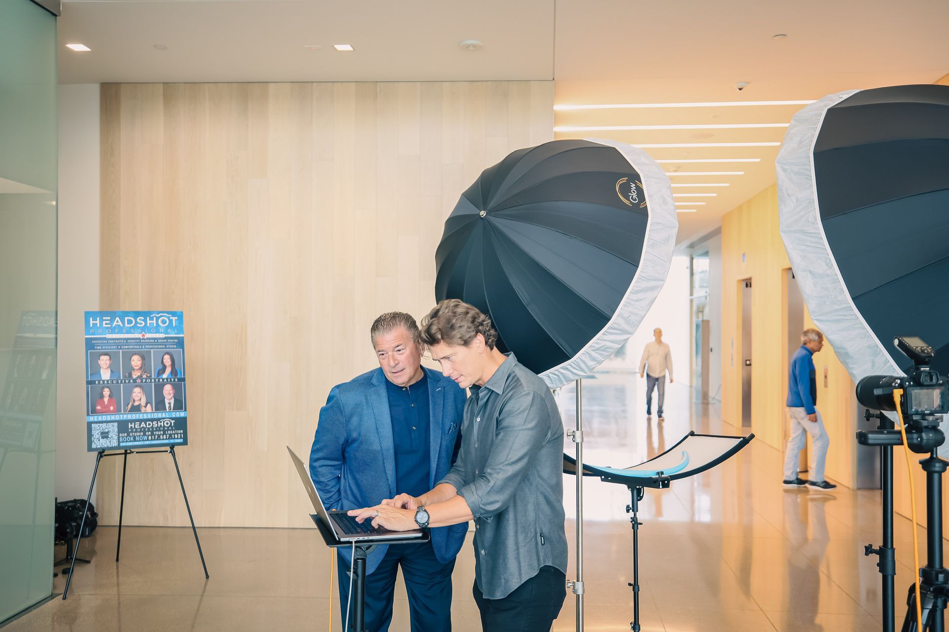 Two men are standing next to each other in a room looking at a laptop.