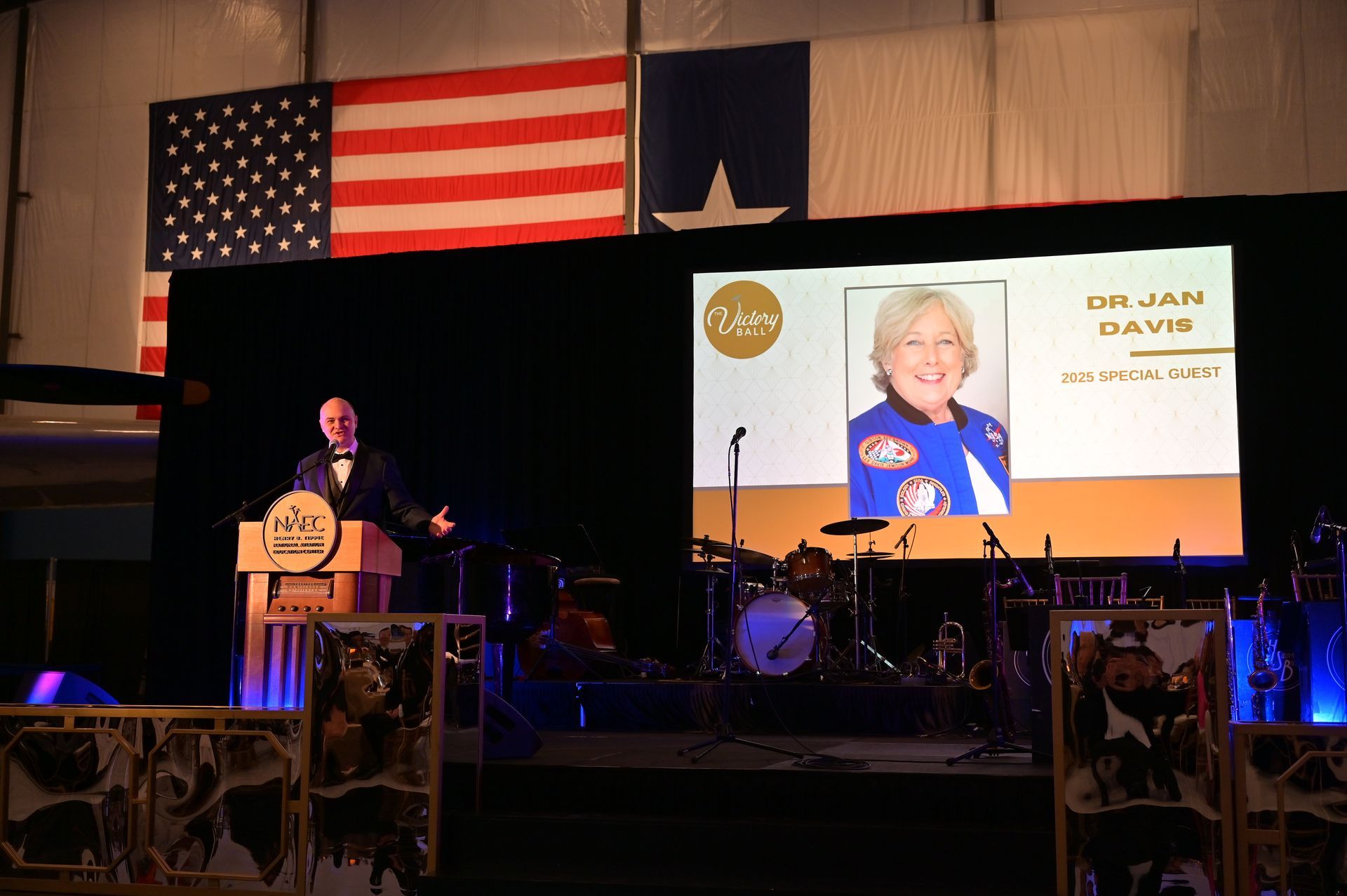 A man stands at a podium in front of a large screen with a picture of a woman on it.