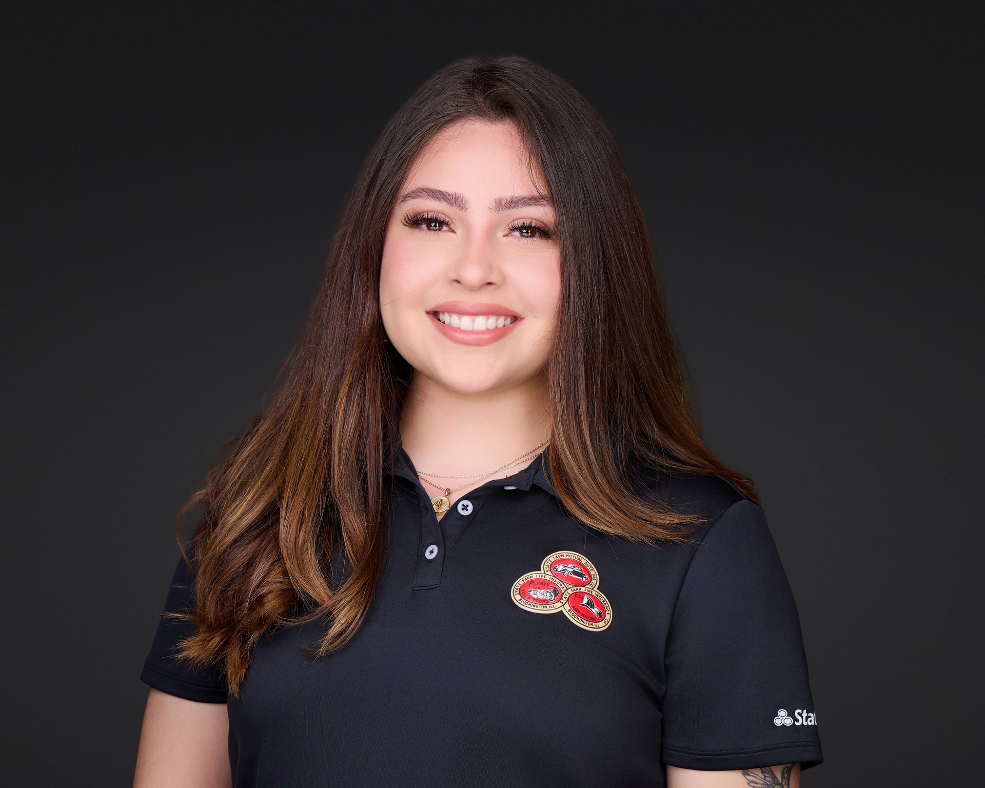 Portrait of a smiling person in a black polo shirt with a red floral logo on a dark background