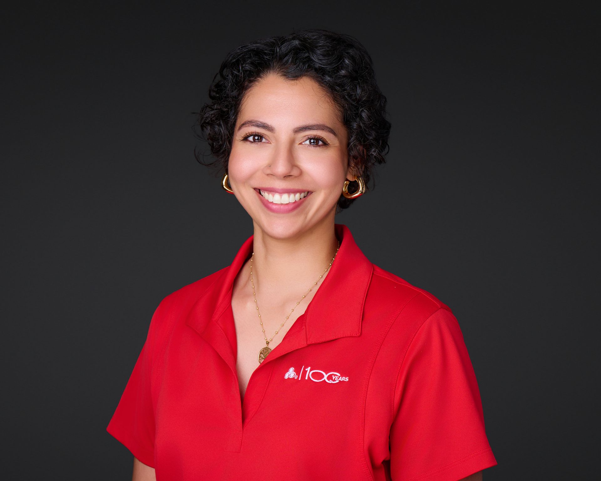 Smiling person in a red polo shirt against a dark background