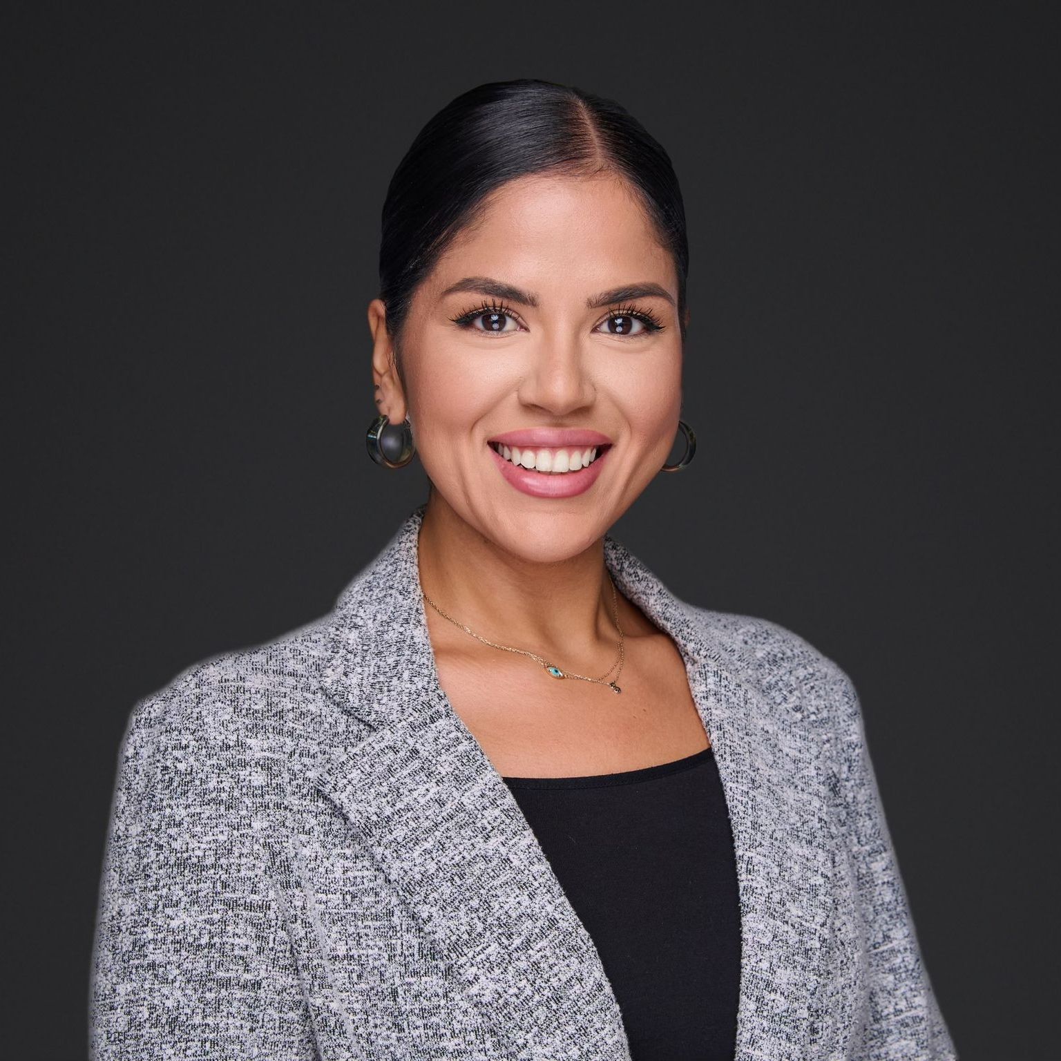 Smiling woman in gray blazer and black top against a dark background