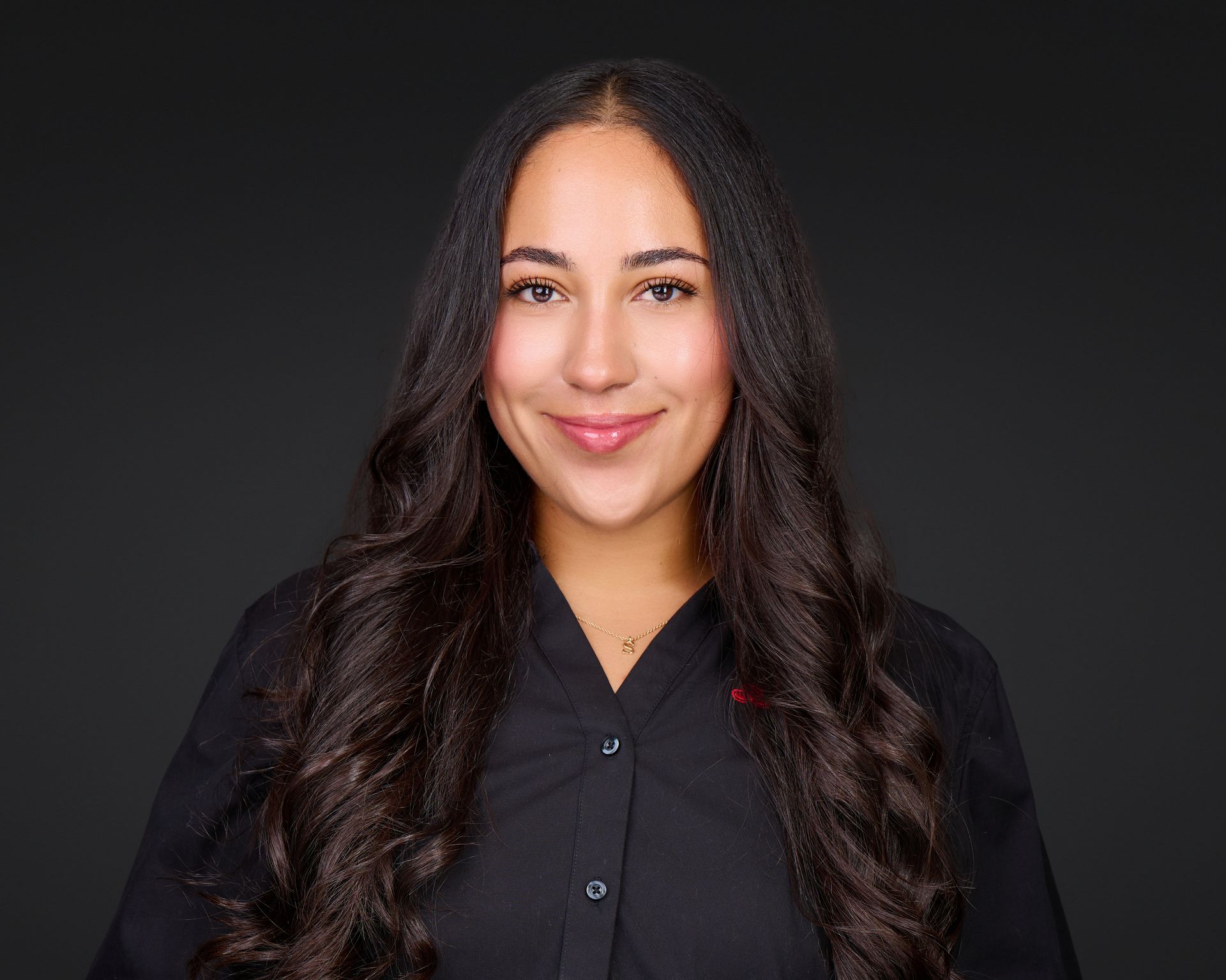 Portrait of a smiling person with long dark hair, wearing a black shirt against a dark background