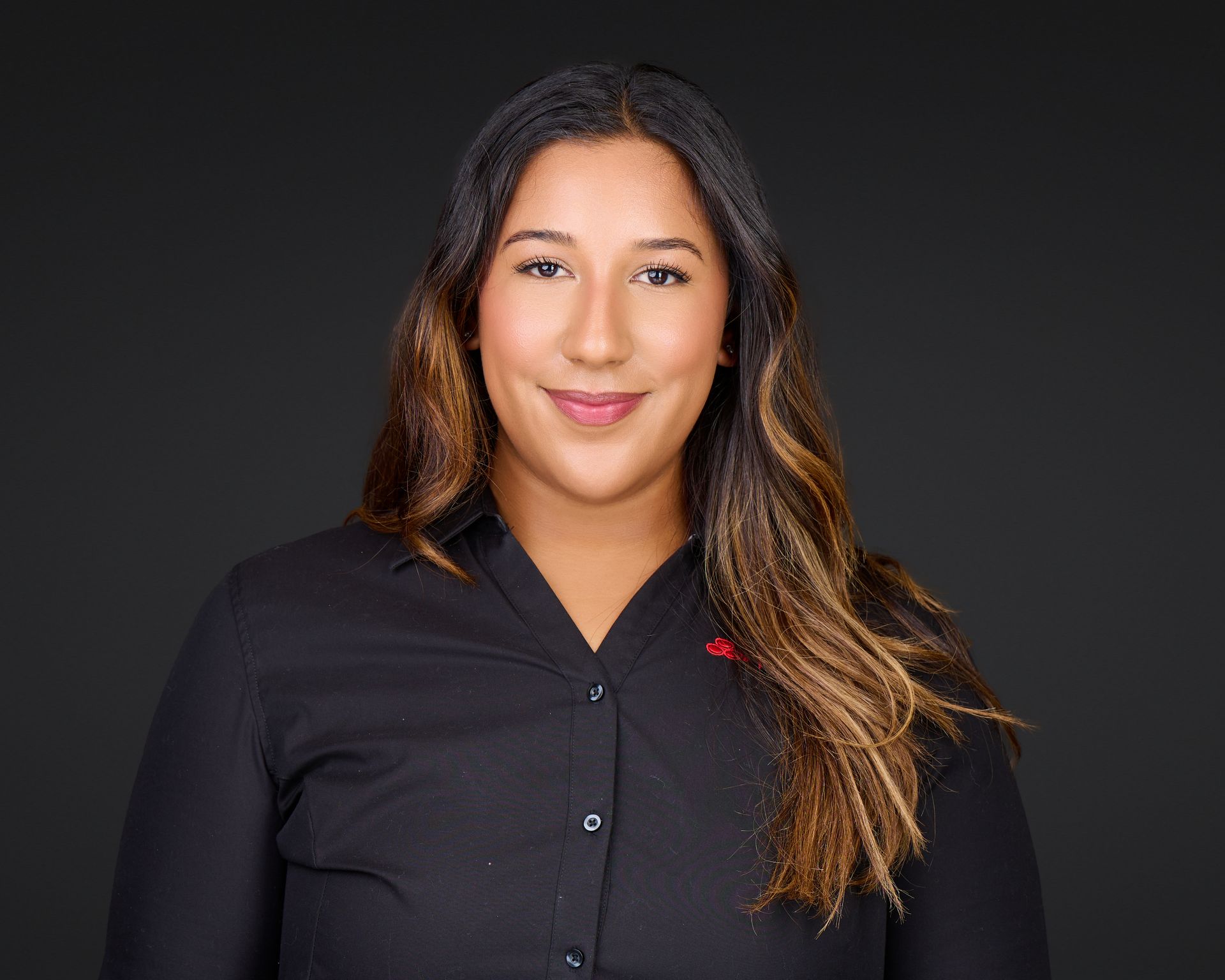 Studio portrait of a woman in a black shirt, facing forward and smiling against a dark background