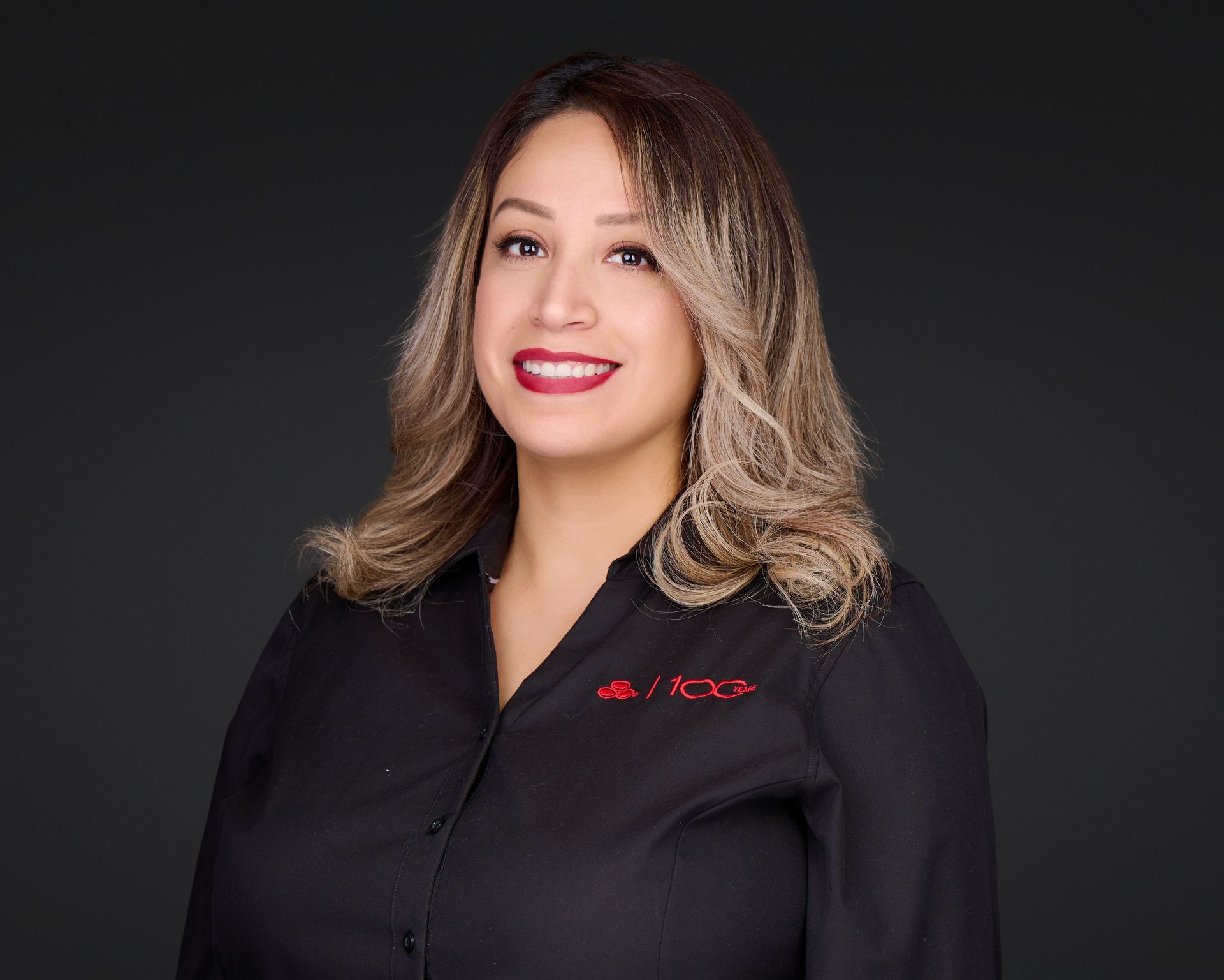 Smiling woman in a black shirt with red logo against a dark background