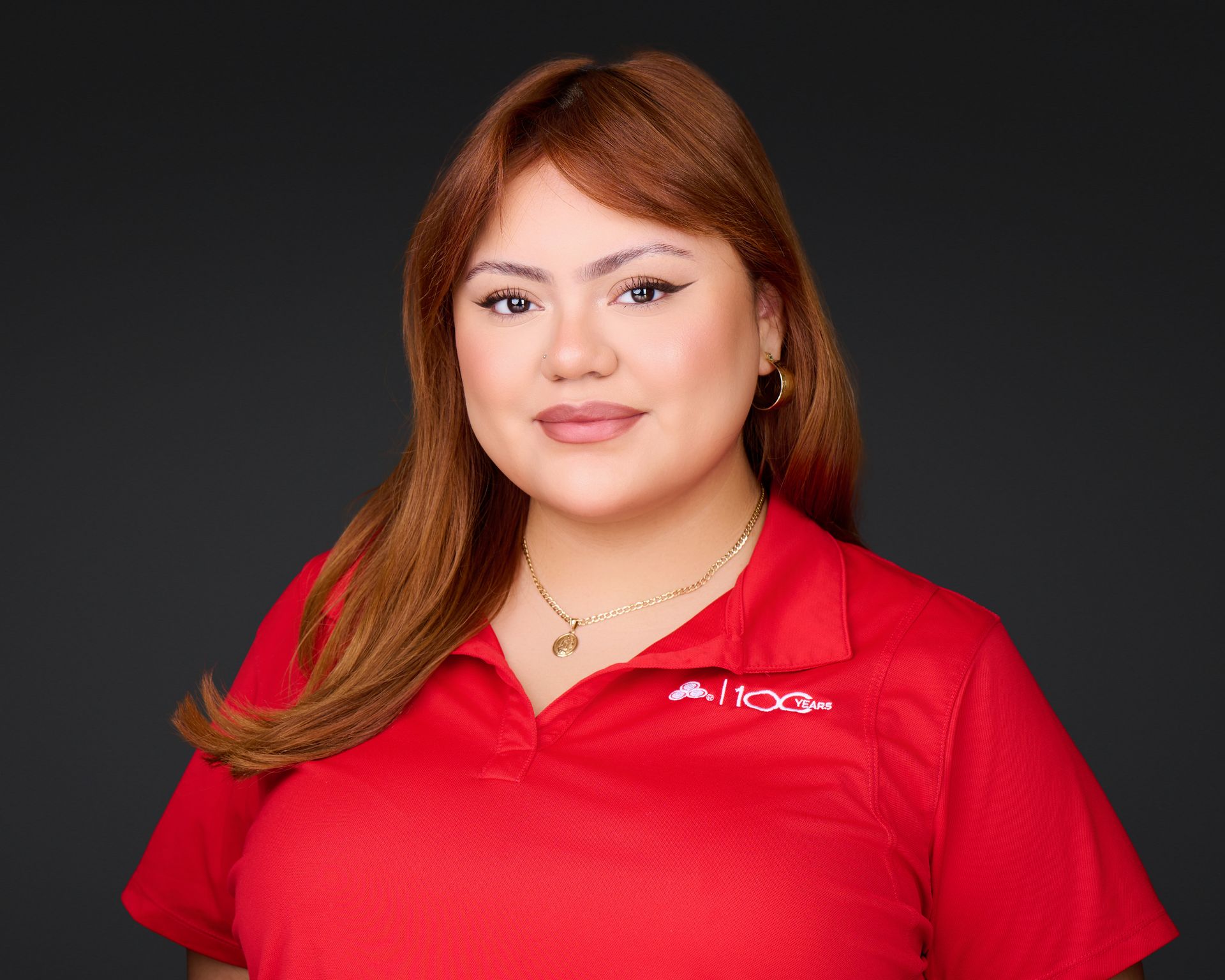 Woman in a red polo shirt smiling against a dark gray background.