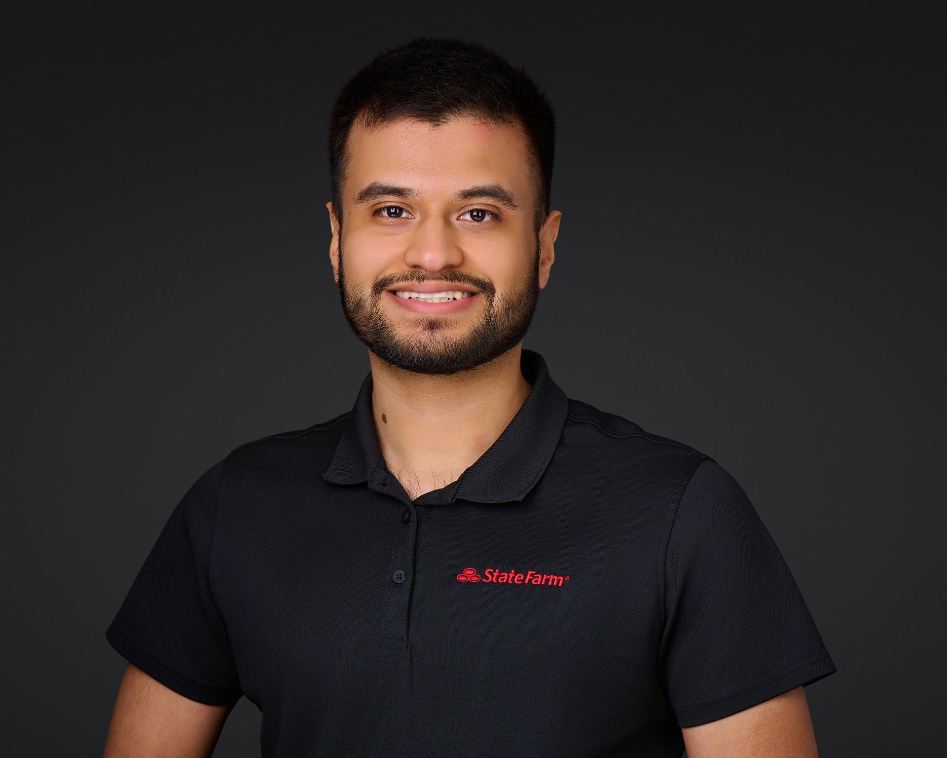 Smiling man in a black polo shirt with a red logo against a dark background