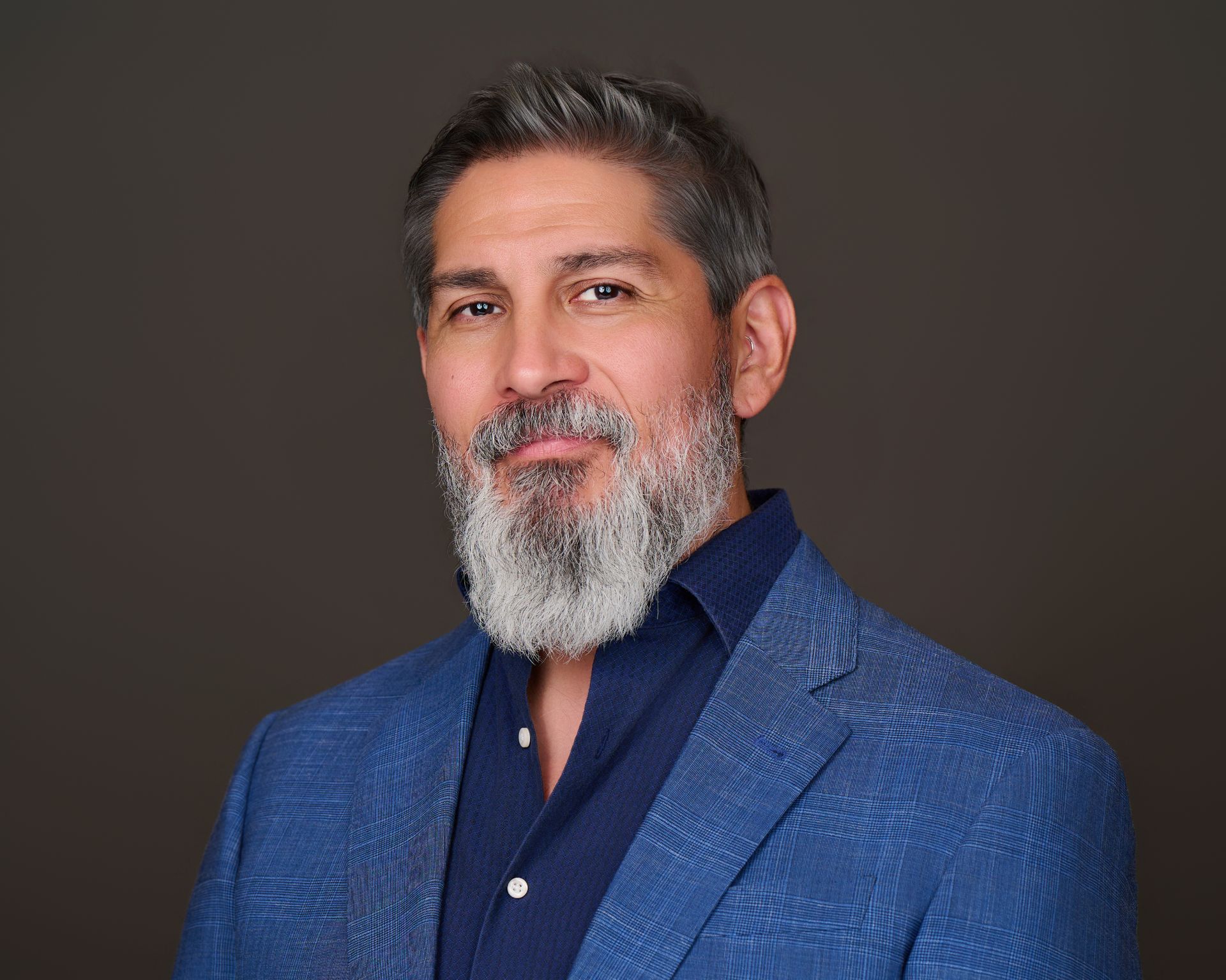 Portrait of a smiling man with a gray beard wearing a blue jacket against a dark background