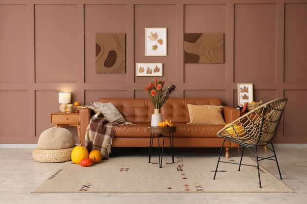 Cozy living room with tan sofa, patterned chairs, soft pink paneled wall art, and fall decor on a light rug
