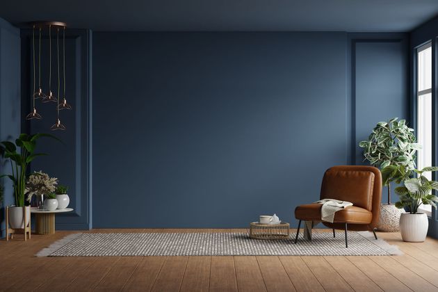 Modern living room with blue wall, leather chair, plants, and a woven rug by large windows