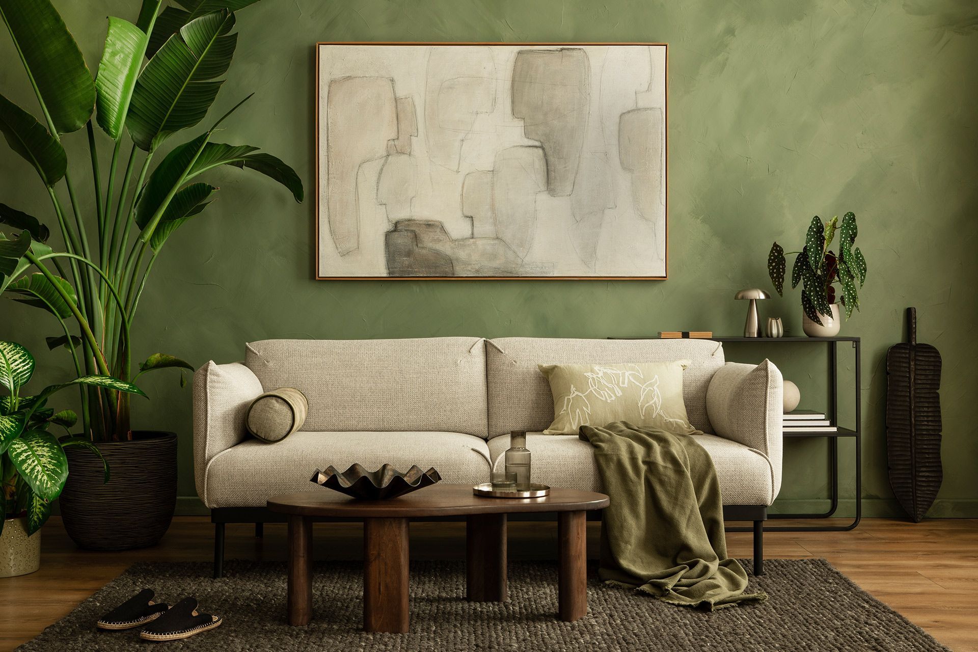 Cozy beige living room with sofa, coffee table, abstract art, plants, and textured green walls.