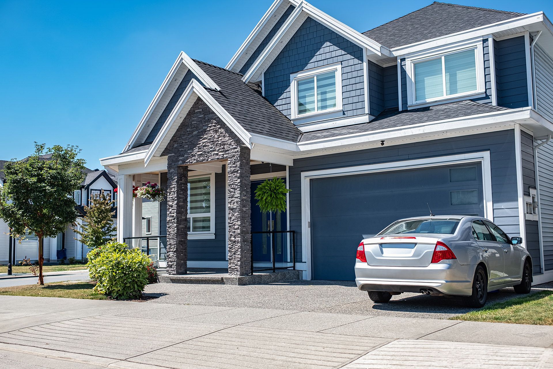 Suburban house with a silver car parked in the driveway under a blue sky
