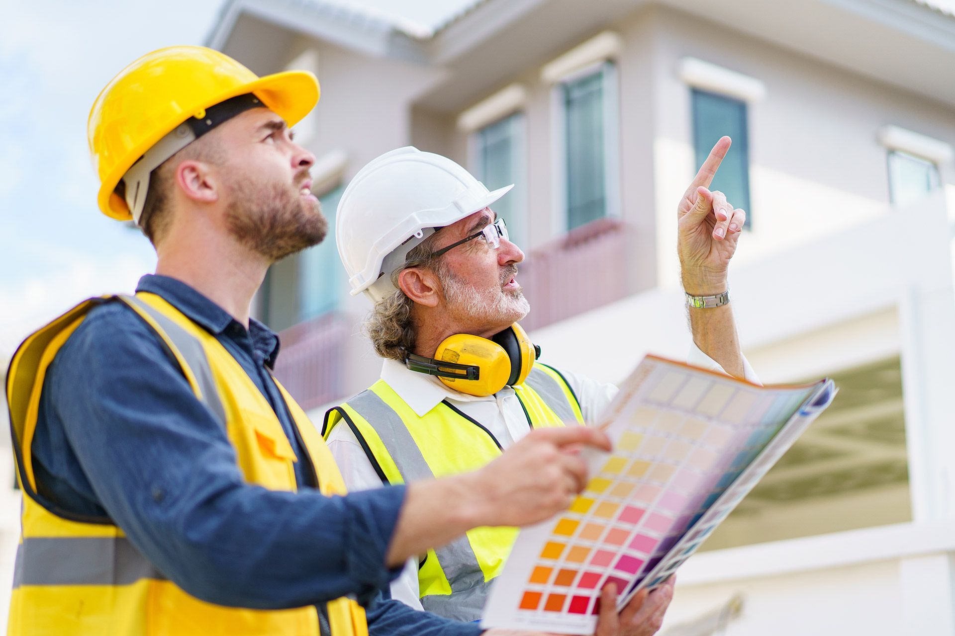 Two construction workers in hard hats reviewing plans and pointing at a building site