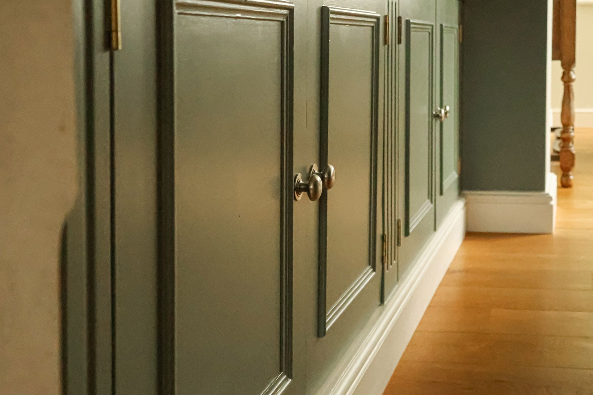 Gray paneled cabinets along a hallway with a light wood floor
