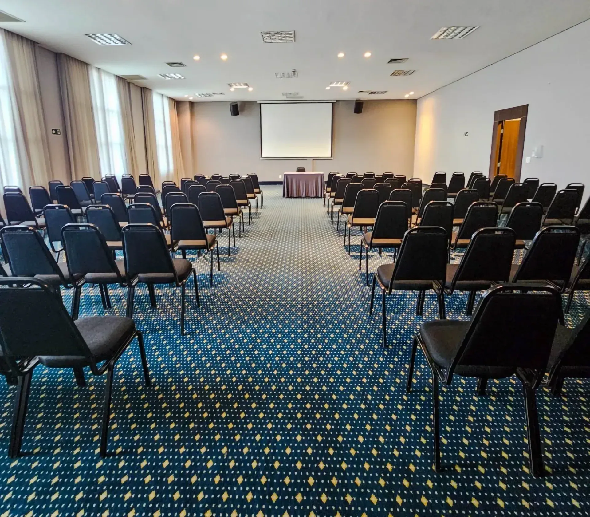 Uma sala de conferências com fileiras de cadeiras e uma tela de projetor