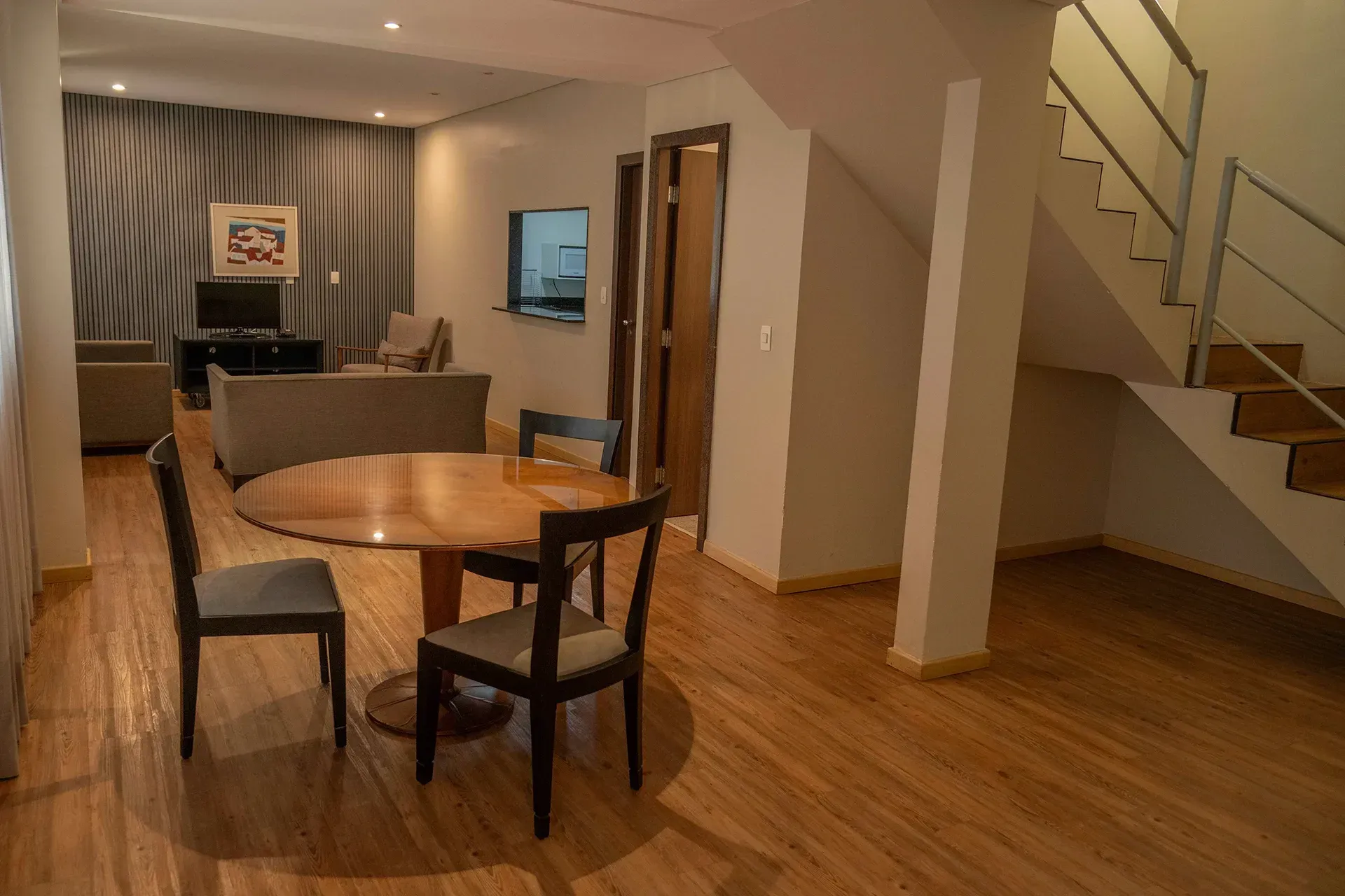 Uma sala de estar com mesa, cadeiras e escadas.