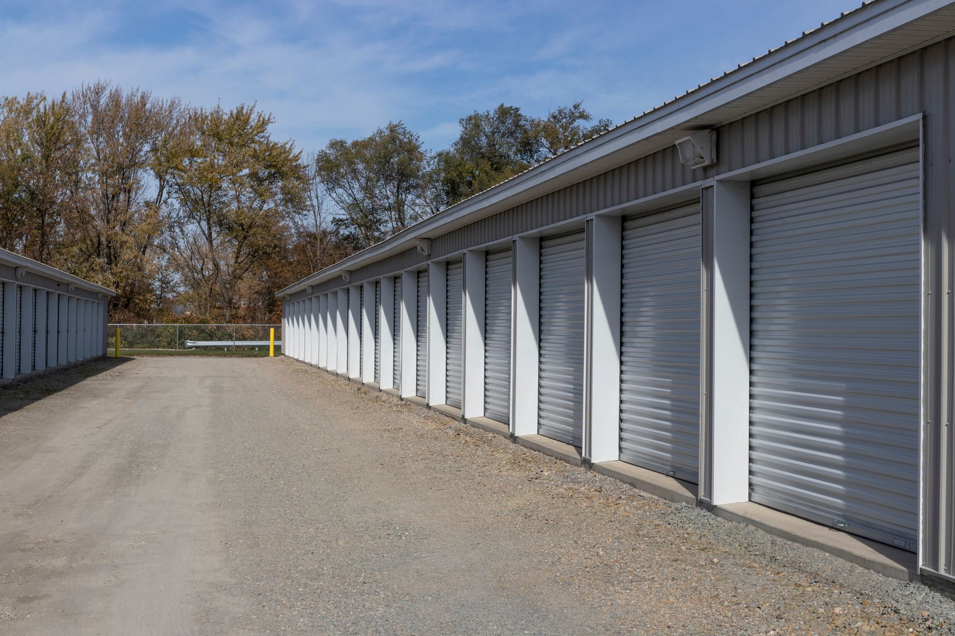 Mini storage units with roll-up doors lining a gravel drive. Mini storage units with roll-up doors lining a gravel drive.