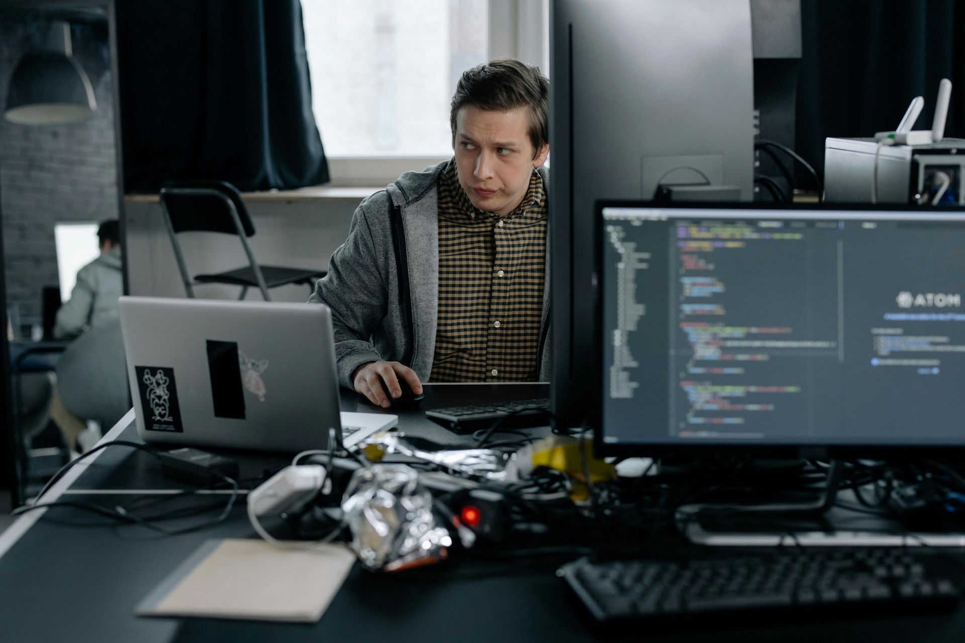 Un homme est assis à un bureau avec un ordinateur portable et deux écrans d'ordinateur.