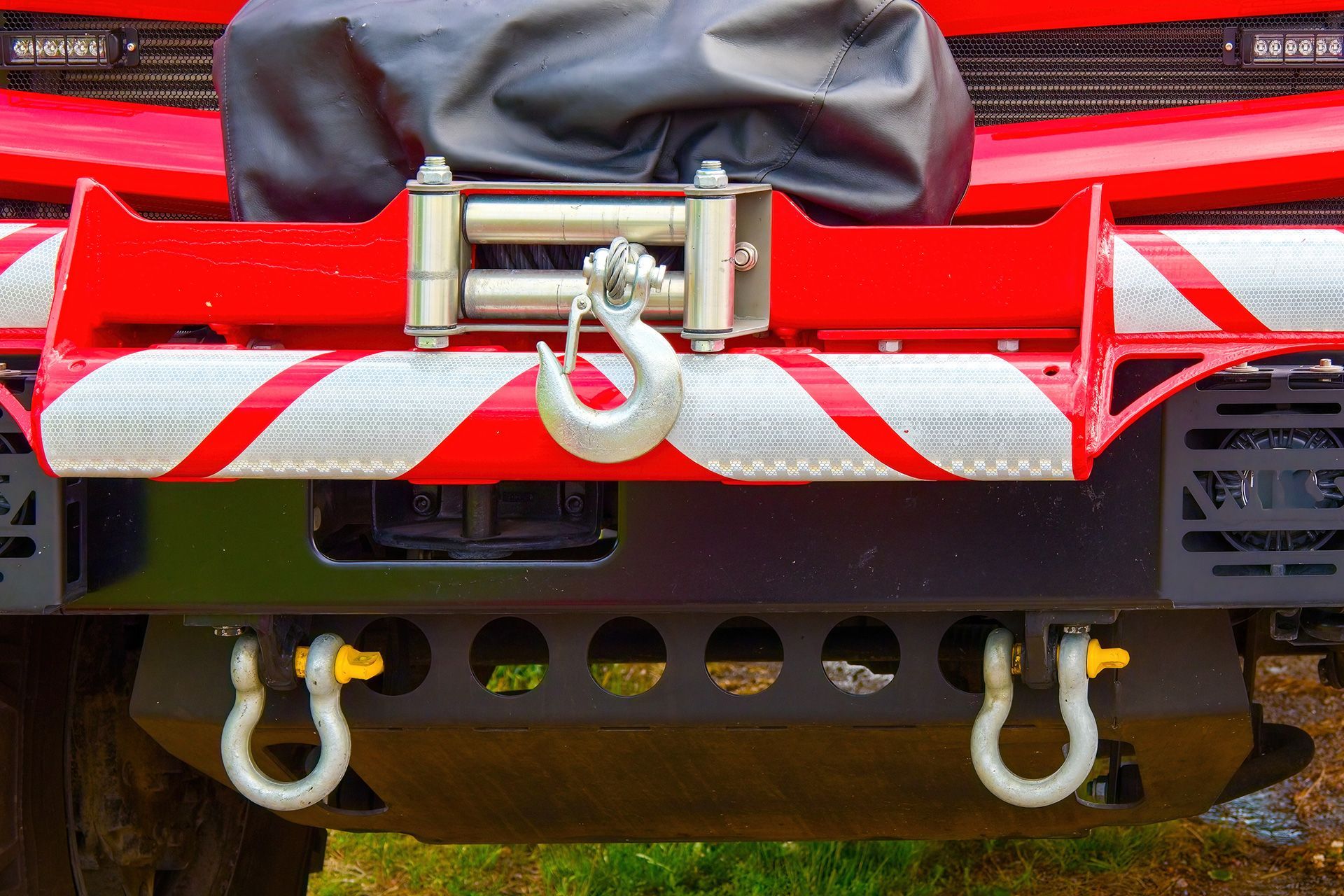 Close-up of a heavy-duty electric winch with a steel hook mounted on the front bumper of a red rescue vehicle