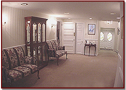 Quiet lobby with patterned chairs, display cabinet, small table, and double doors at the back.