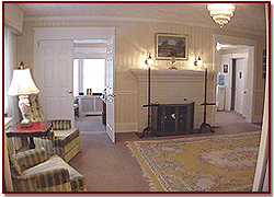 Living room with fireplace, patterned chairs, lamp, and doorway to adjoining room