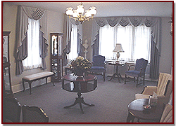 Elegant living room with sofas, chairs, chandelier, and large curtained windows