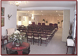 Empty banquet hall with rows of chairs, white walls, and a small floral table in the foreground