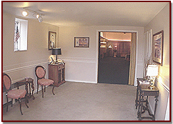 Empty beige living room with chairs, table lamps, and an open doorway to a darker room