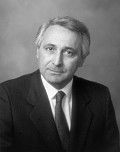 Black-and-white portrait of a man in a suit and tie, facing the camera with a serious expression