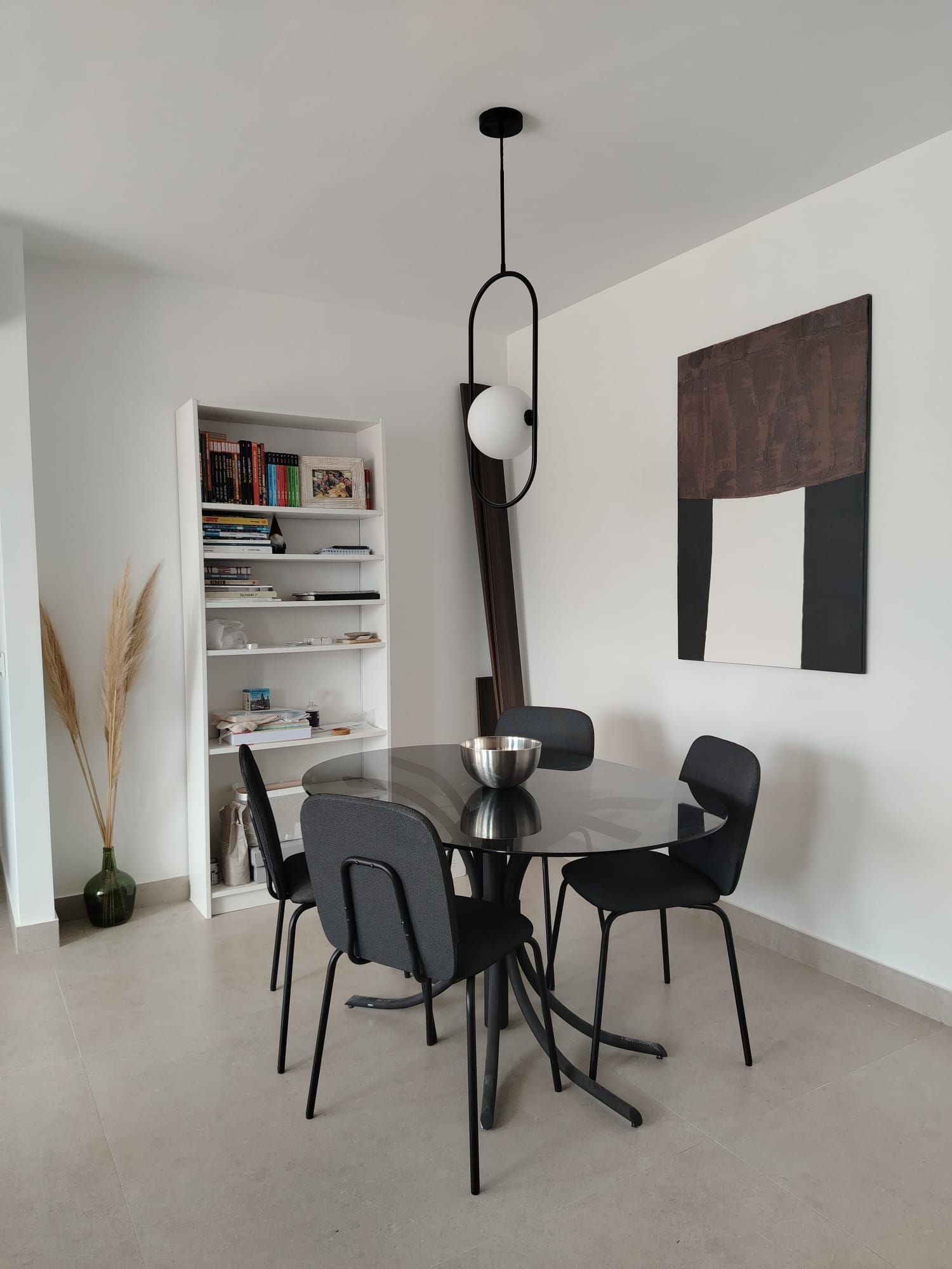 Comedor moderno con mesa y sillas negras, estantes blancos y arte abstracto en la pared.