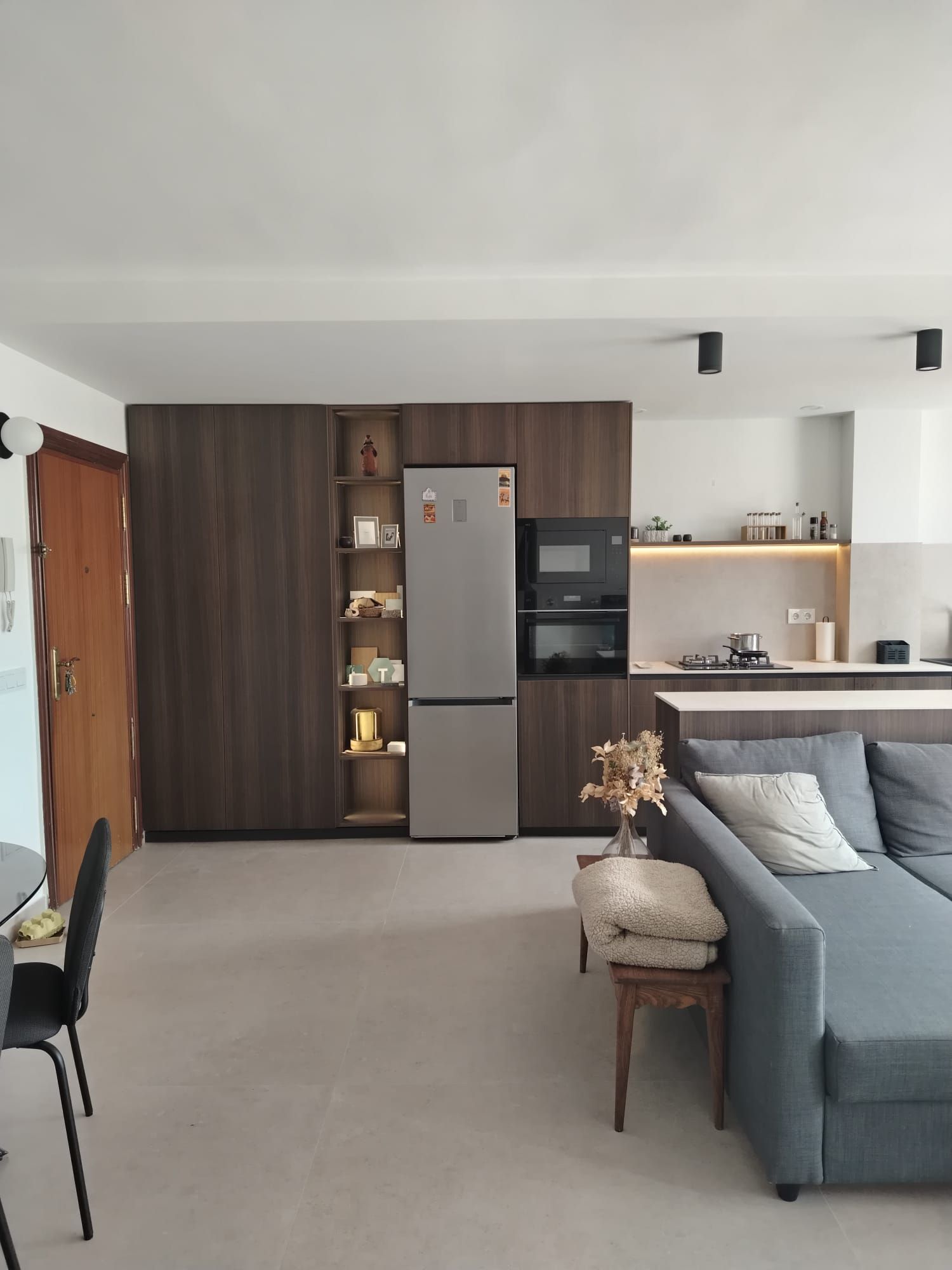 Sala de estar moderna con sofá gris, mesa de comedor y área de cocina al fondo.