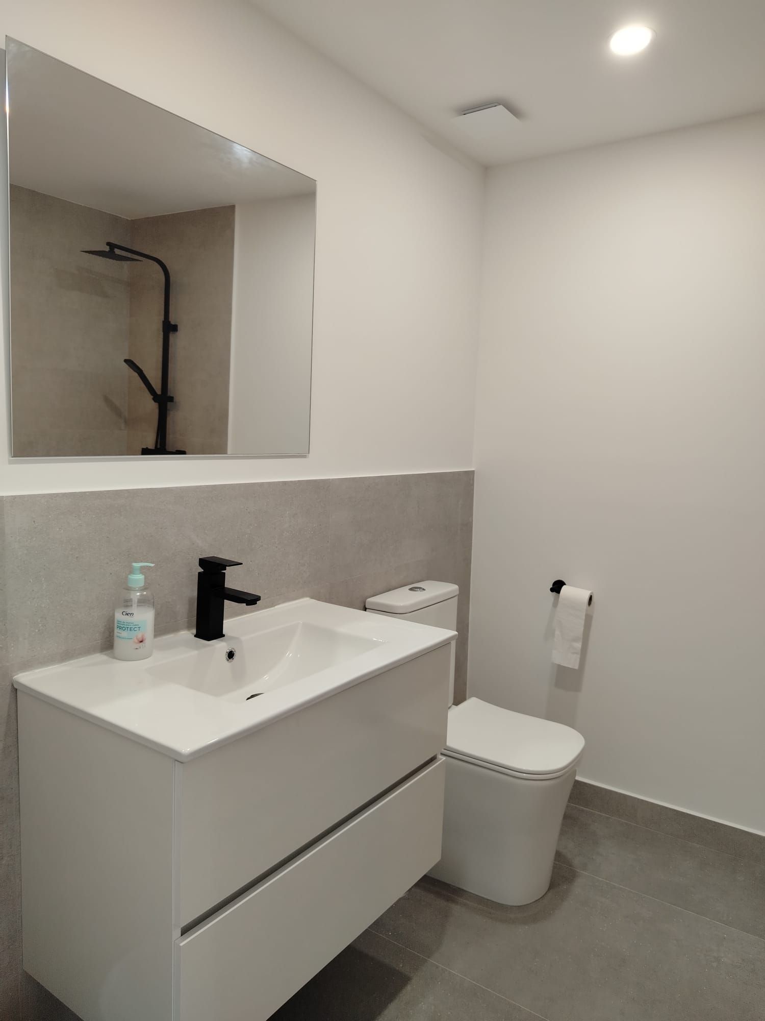 Baño moderno de color blanco con lavabo, espejo, inodoro y ducha a ras de suelo con reflejo.