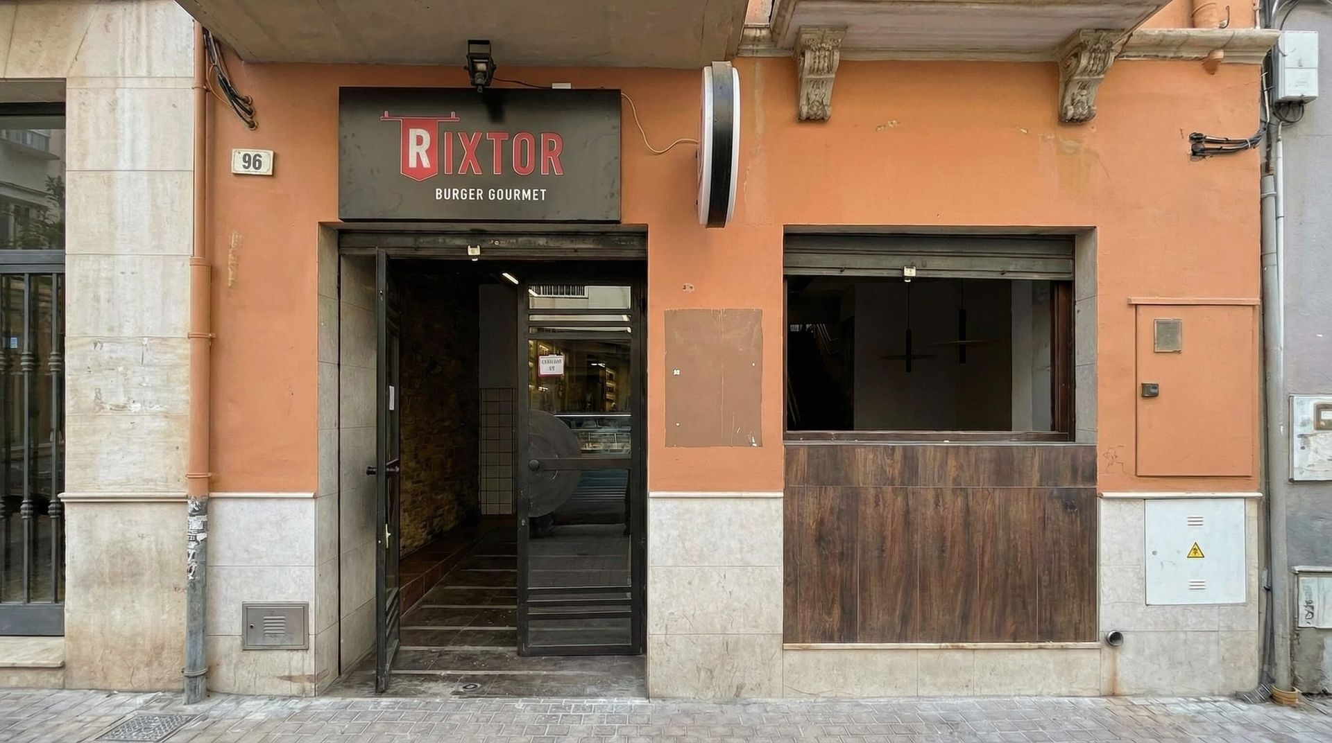 Local comercial con fachada naranja, puerta abierta y ventanilla de servicio de madera bajo un letrero que dice “RIBO”.