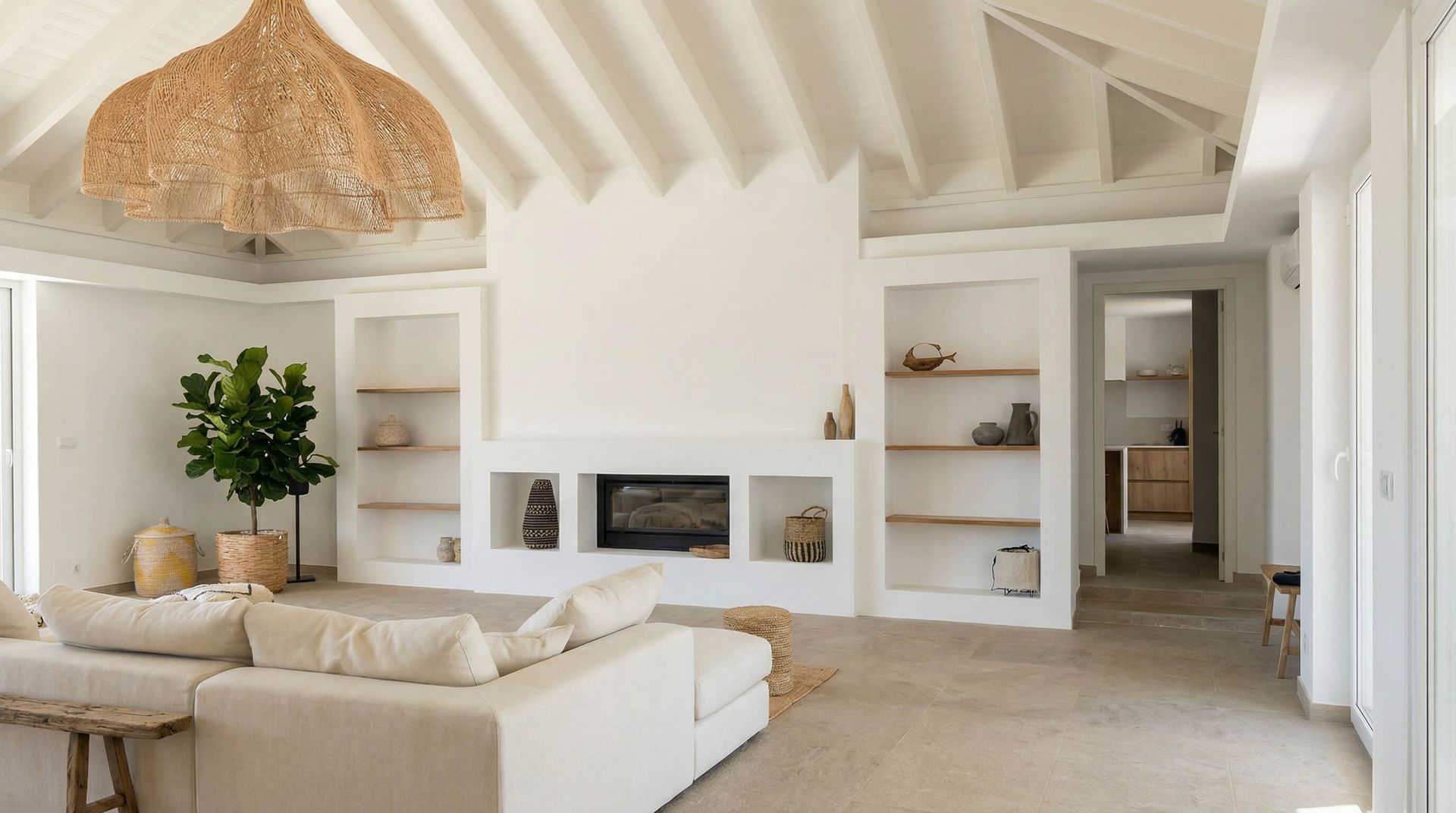 Sala de estar blanca y luminosa con sofá modular, estanterías empotradas, chimenea y lámpara colgante tejida.