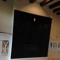 A sleek black fireplace wall with a modern hearth, flanked by white decorative cabinetry under rustic wooden ceiling beams.