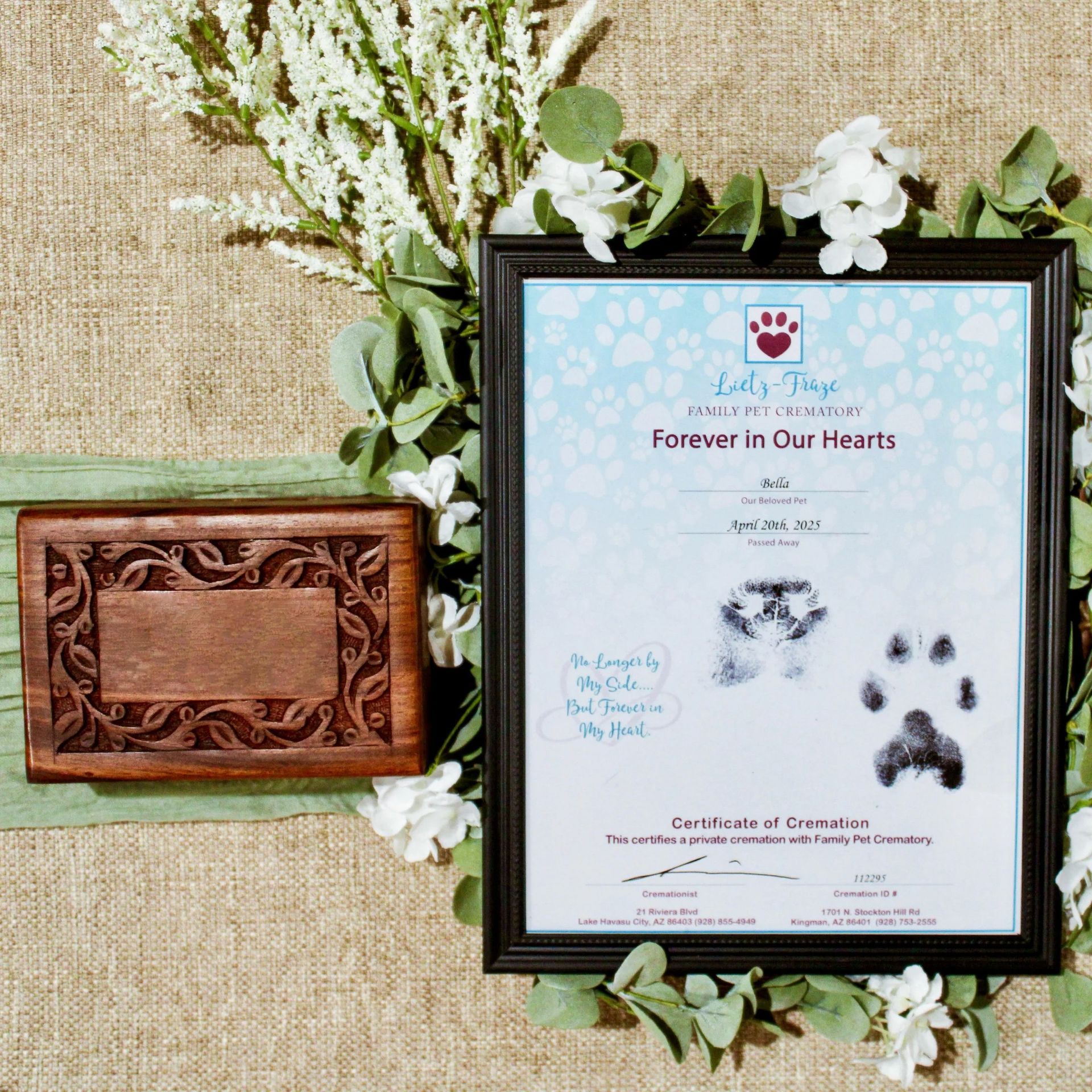 Pet memorial display with framed paw-print tribute and carved wooden plaque on burlap with flowers